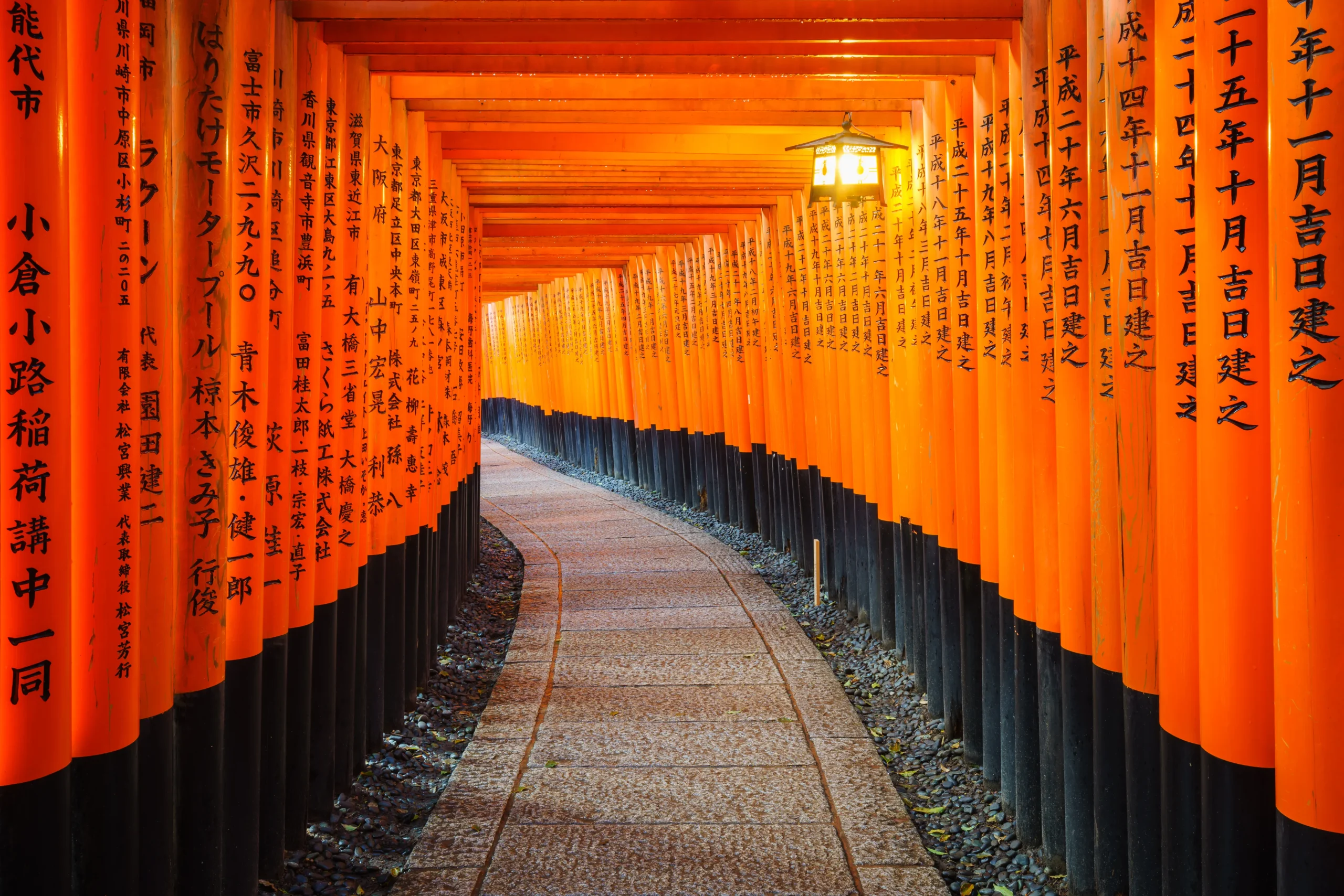 Endless rows of vibrant orange torii gates form a tunnel-like path at Kyoto’s Fushimi Inari Taisha, with inscriptions on each pillar.