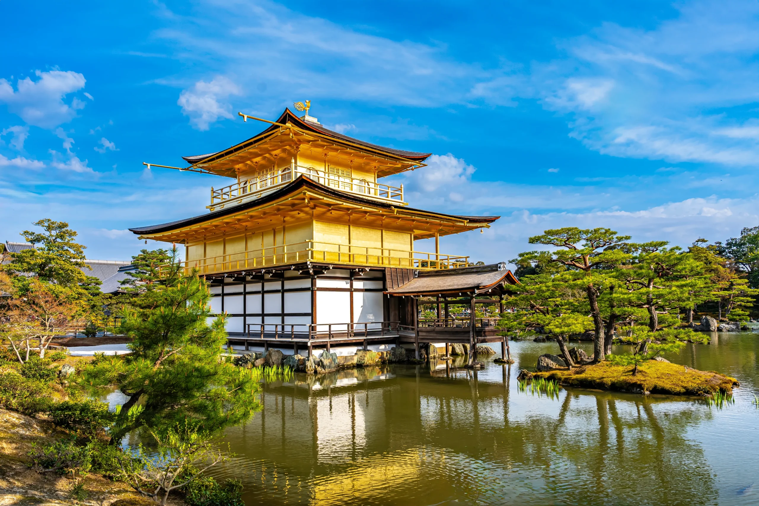 The stunning gold-leaf-covered Kinkaku-ji temple reflected in a serene pond under a bright blue sky in Kyoto, Japan