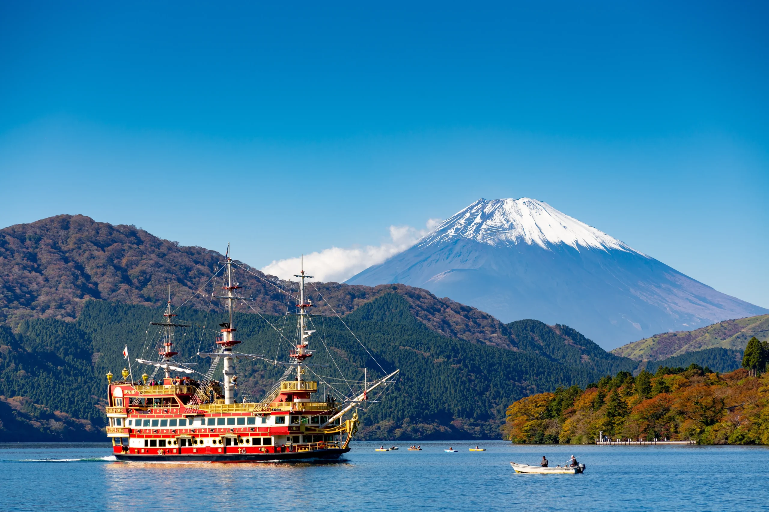 A colorful sightseeing boat sails on Lake Ashi, with the snow-capped peak of Mt. Fuji rising majestically in the background.