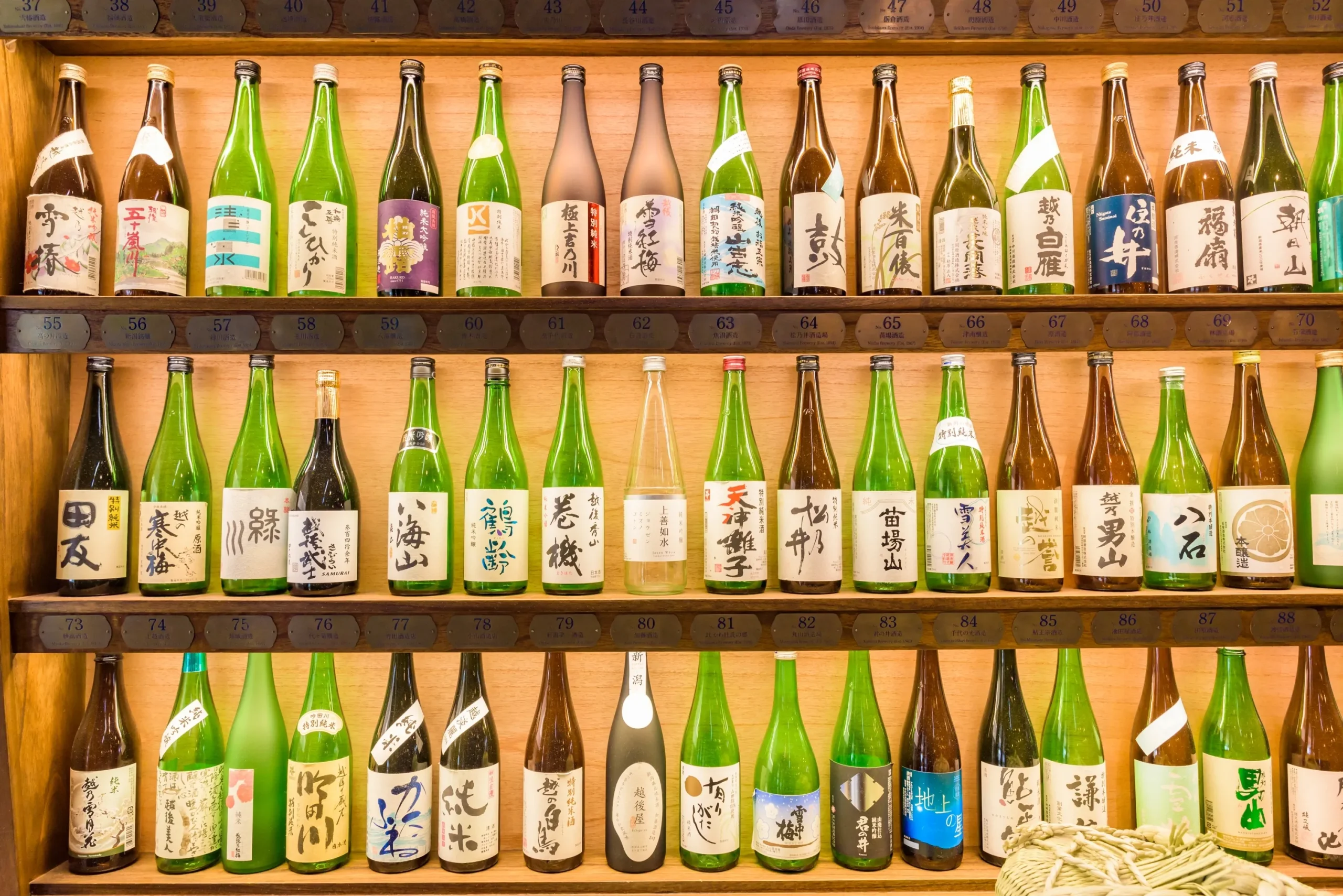 A display of various Japanese sake bottles on wooden shelves, showcasing different labels and brands.