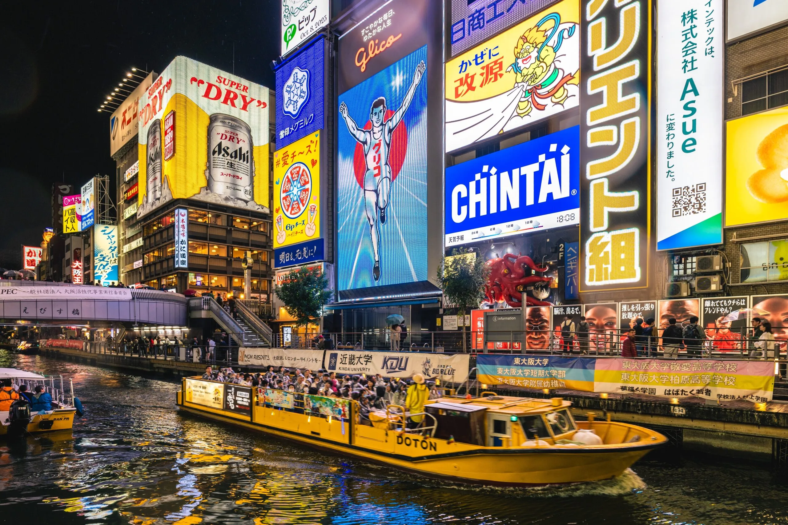 Neon-lit Dotonbori at night with the Glico sign and a sightseeing boat on the canal.