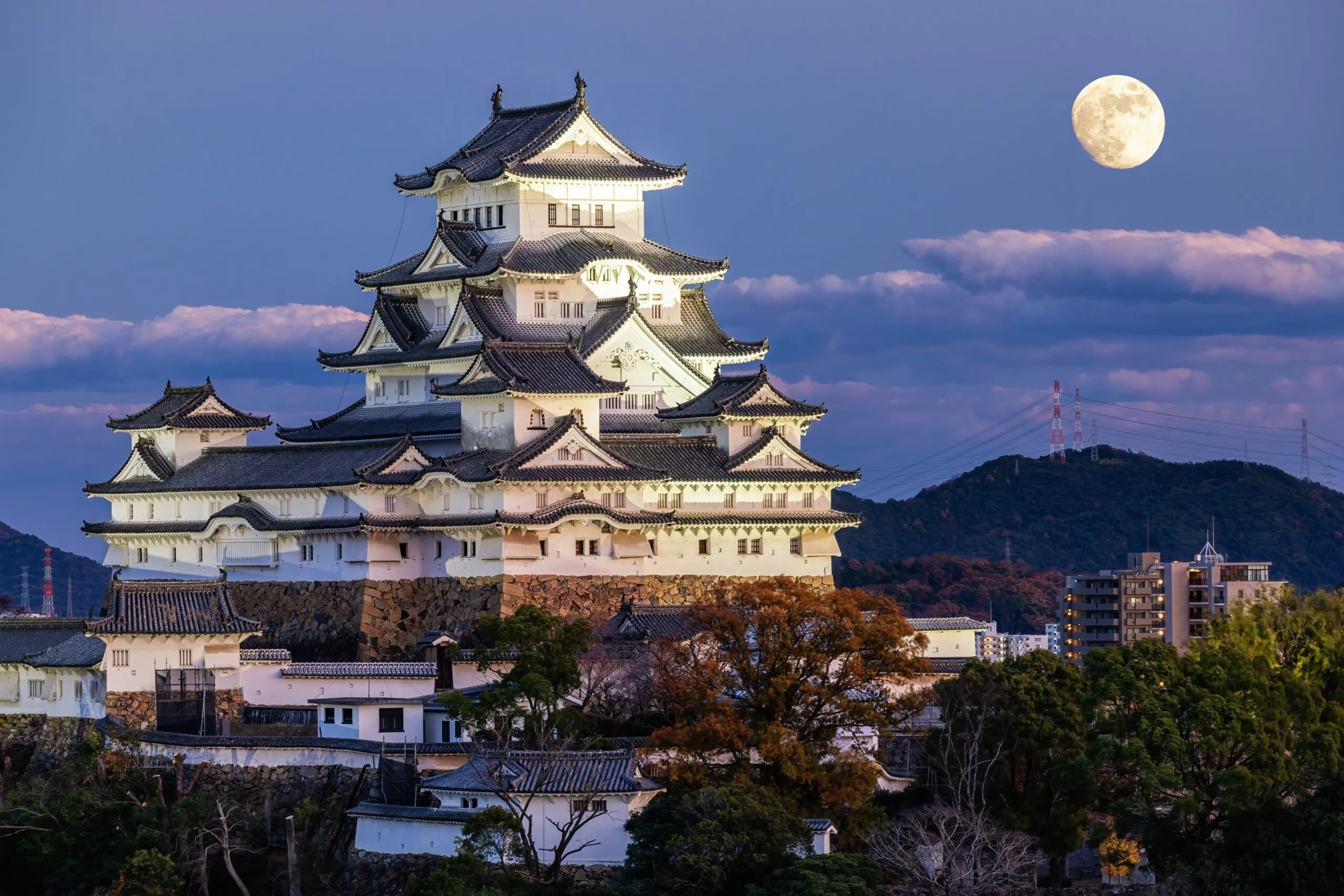 Himeji Castle at dusk with a full moon in the background.