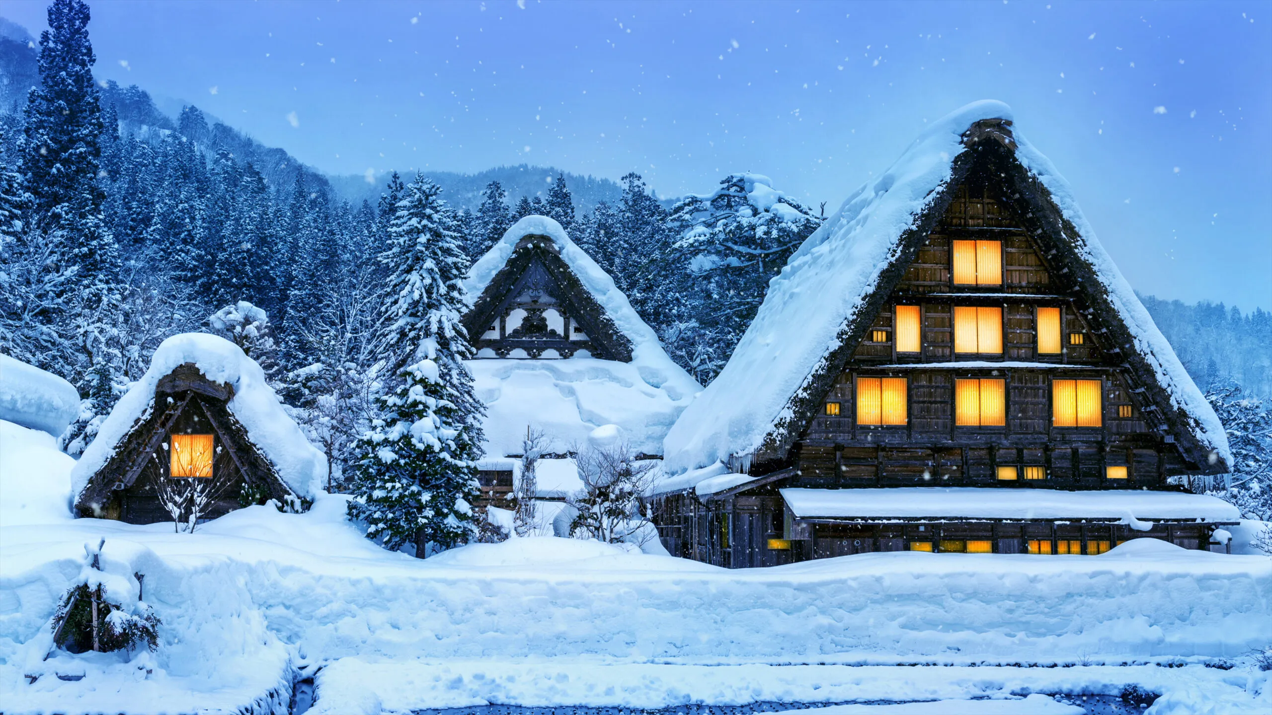 Snow-covered gassho-style houses glowing warmly in Shirakawa-go, Japan.