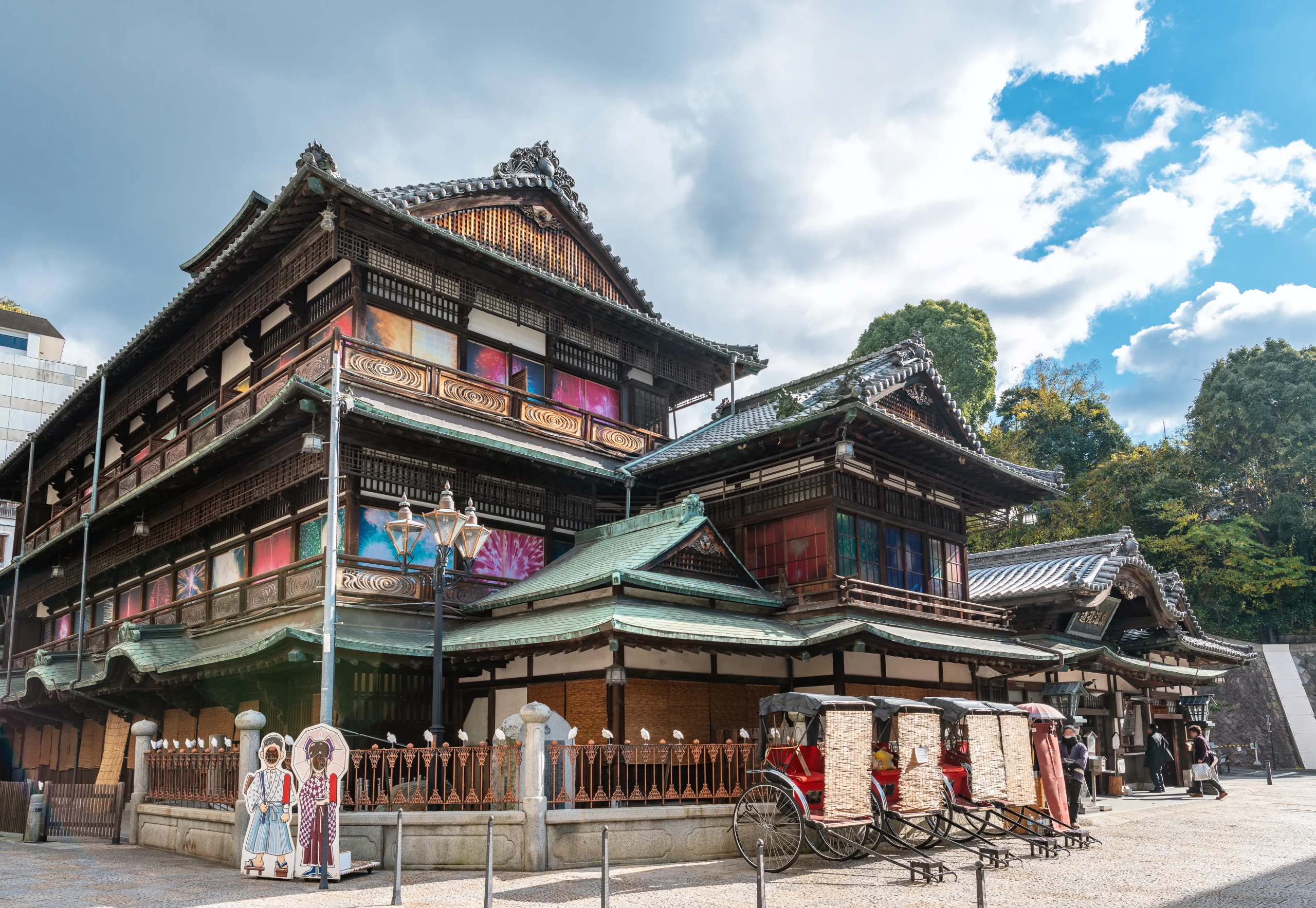 A historic wooden building representing traditional Japanese hot spring culture, with a charming exterior and tourists enjoying photography outside