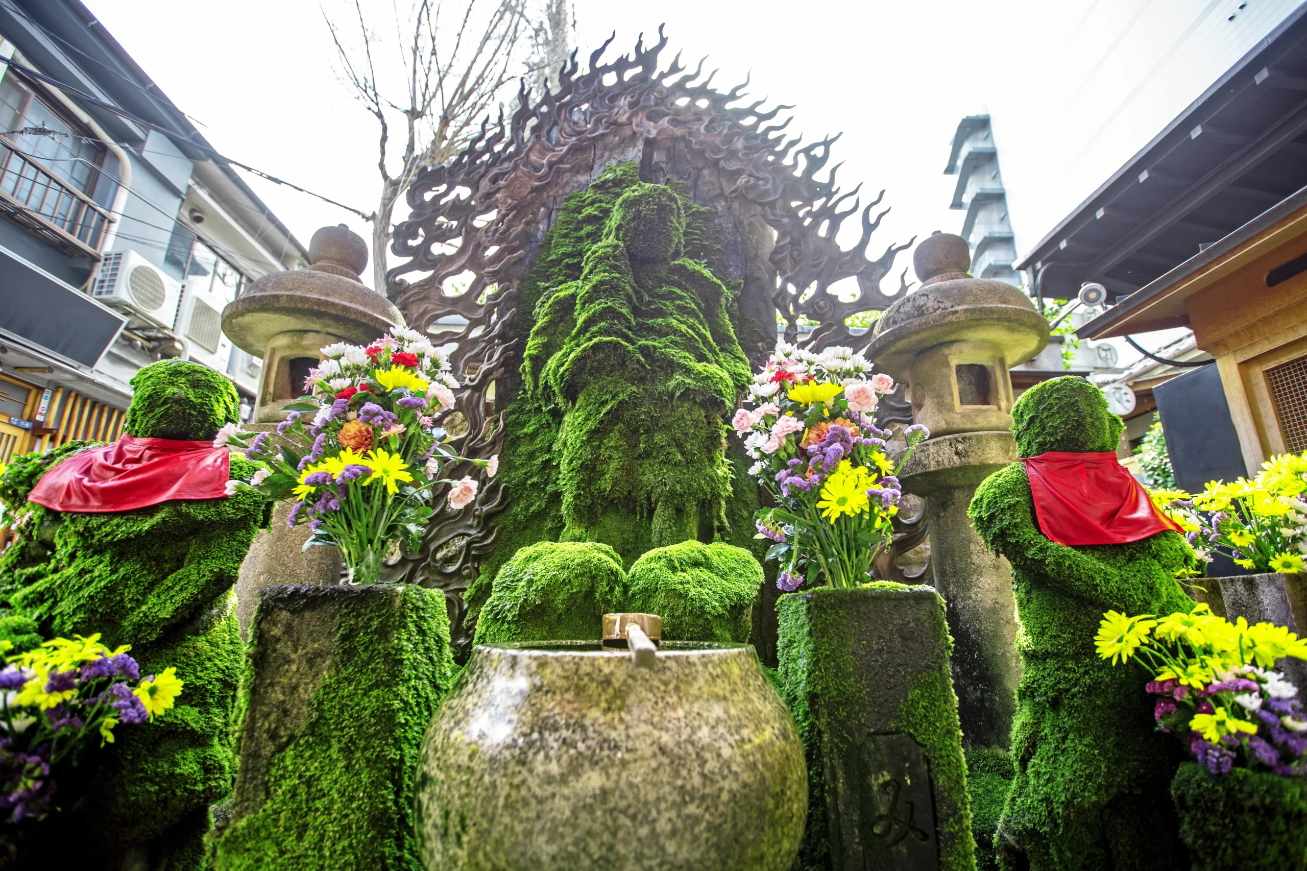 A moss-covered statue of Fudo Myo-o surrounded by colorful flowers at Hozenji Temple