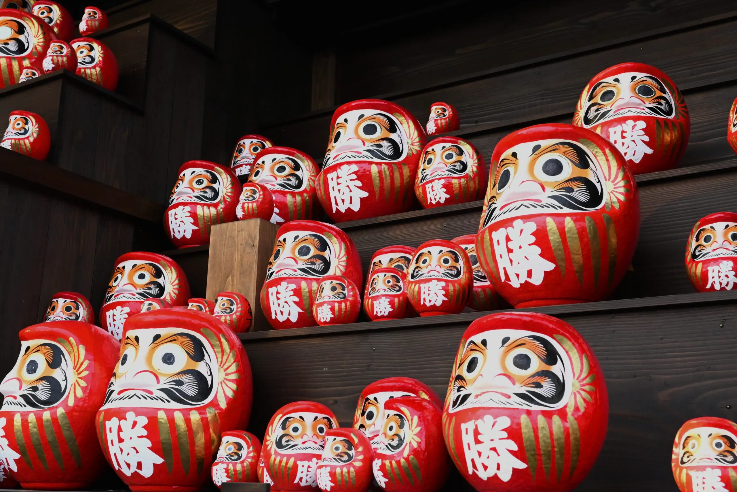 Rows of red Daruma dolls with 'victory' written in Japanese, displayed on wooden steps at Katsuo-ji Temple in Minoh