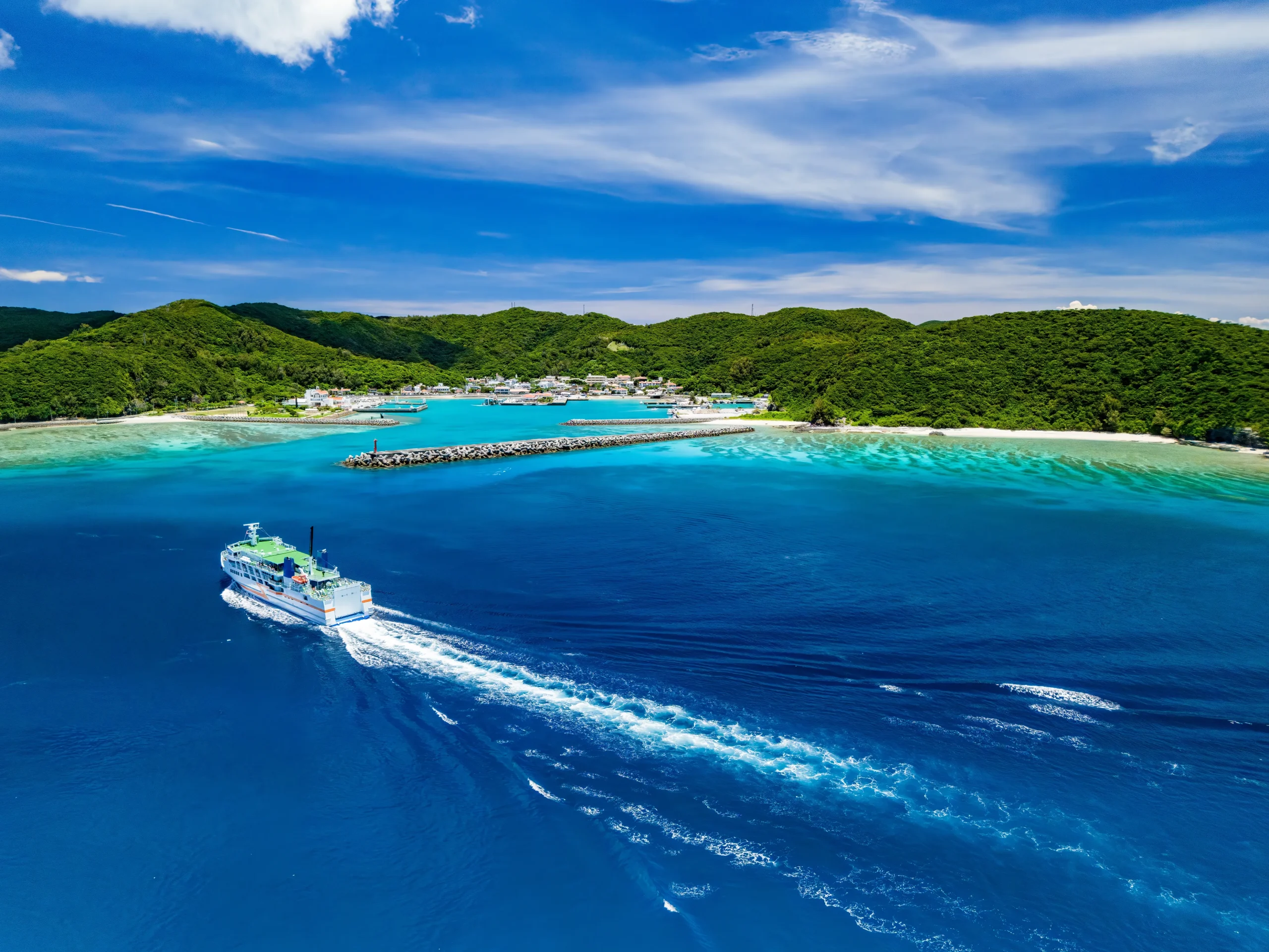Aerial view of the Kerama Islands in Okinawa with crystal-clear turquoise waters, a ferry boat, and lush green islands under a bright summer sky