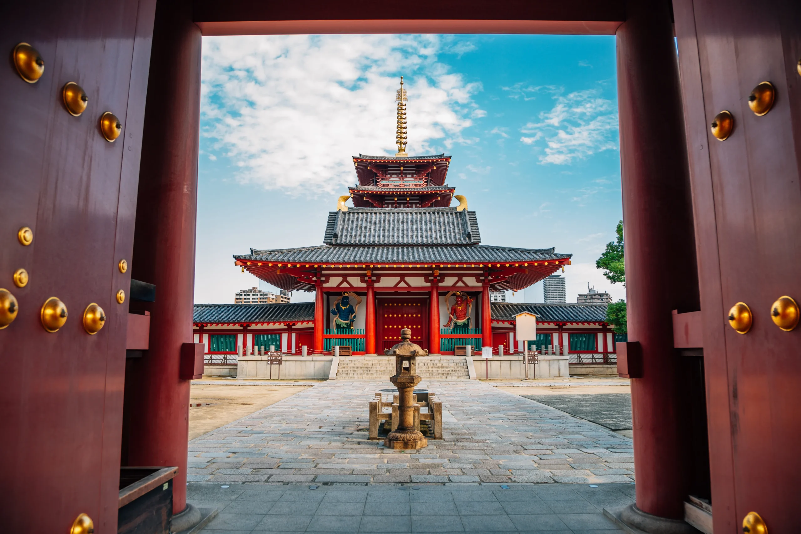 The main entrance gate of Shitennoji Temple, featuring vivid red pillars and golden accents, with a view of the five-story pagoda in the background in Osaka, Japan.