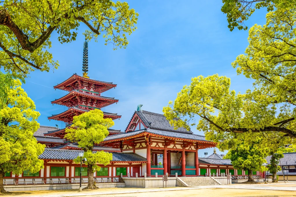 A stunning five-story pagoda and traditional temple architecture framed by lush green trees at Shitennoji Temple in Osaka, Japan