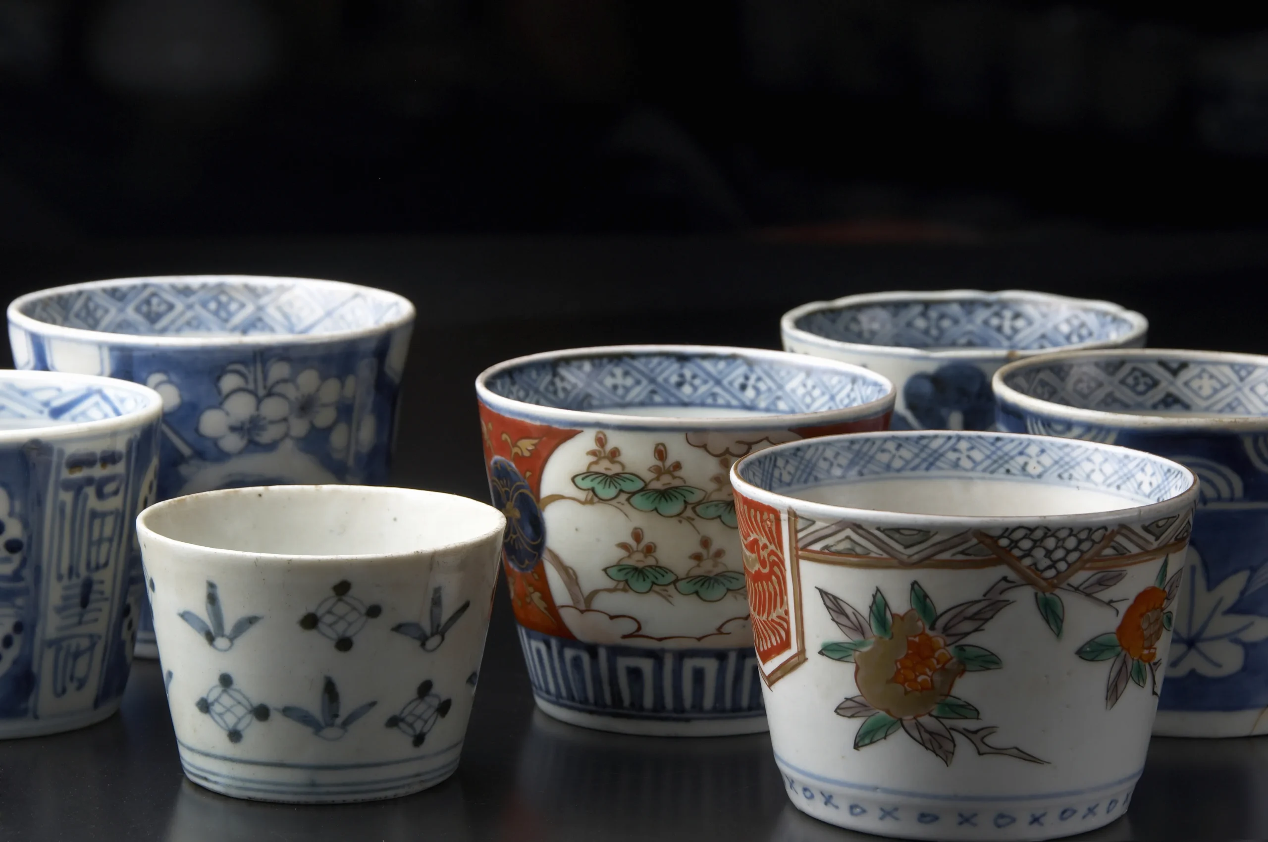 Imari ware cups with a variety of elegant patterns, ranging from blue and white designs to multicolored floral and geometric motifs, displayed under soft lighting.