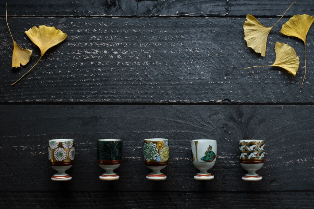 A row of five small Kutani-yaki sake cups, each featuring unique hand-painted designs