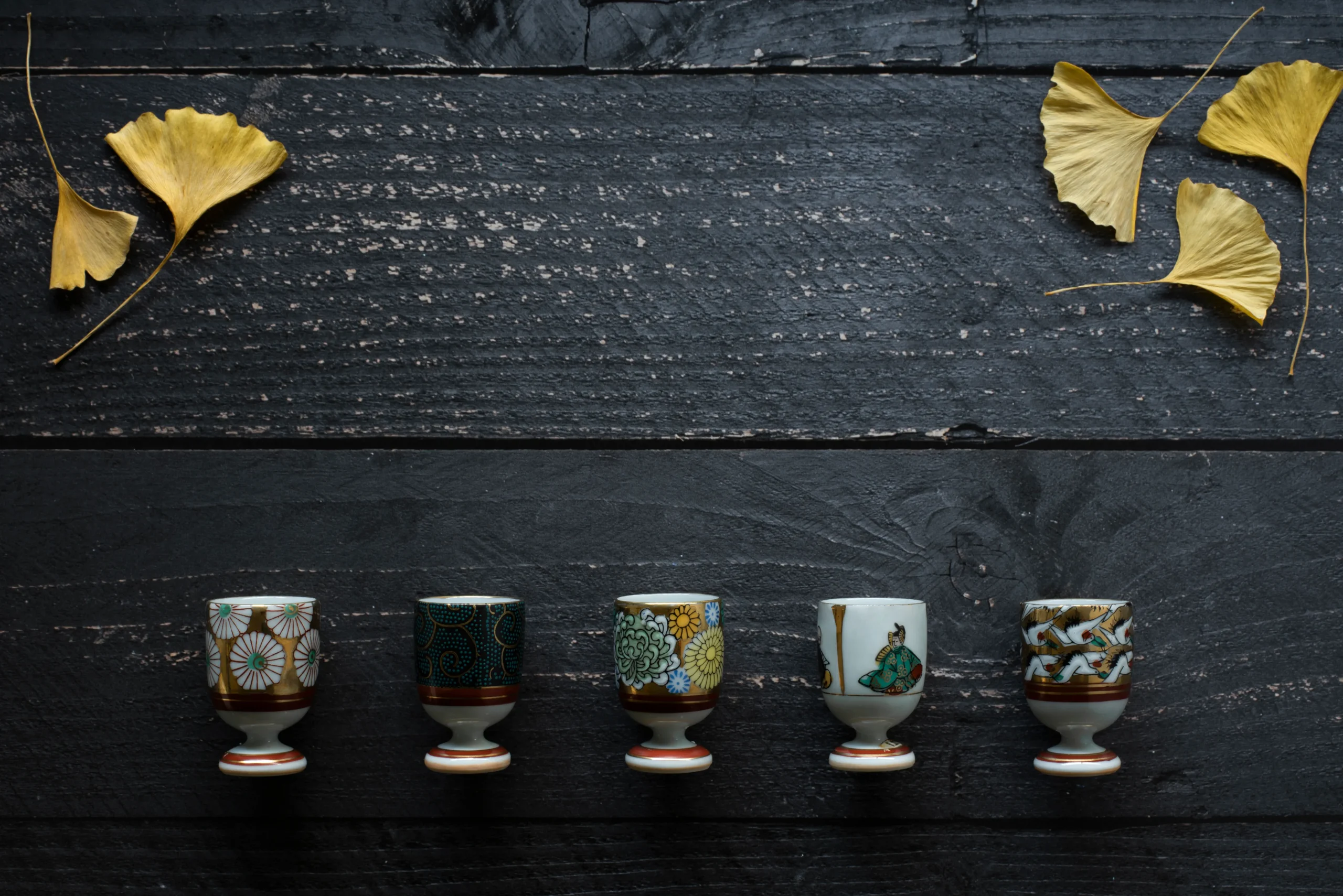 A row of five small Kutani-yaki sake cups, each featuring unique hand-painted designs