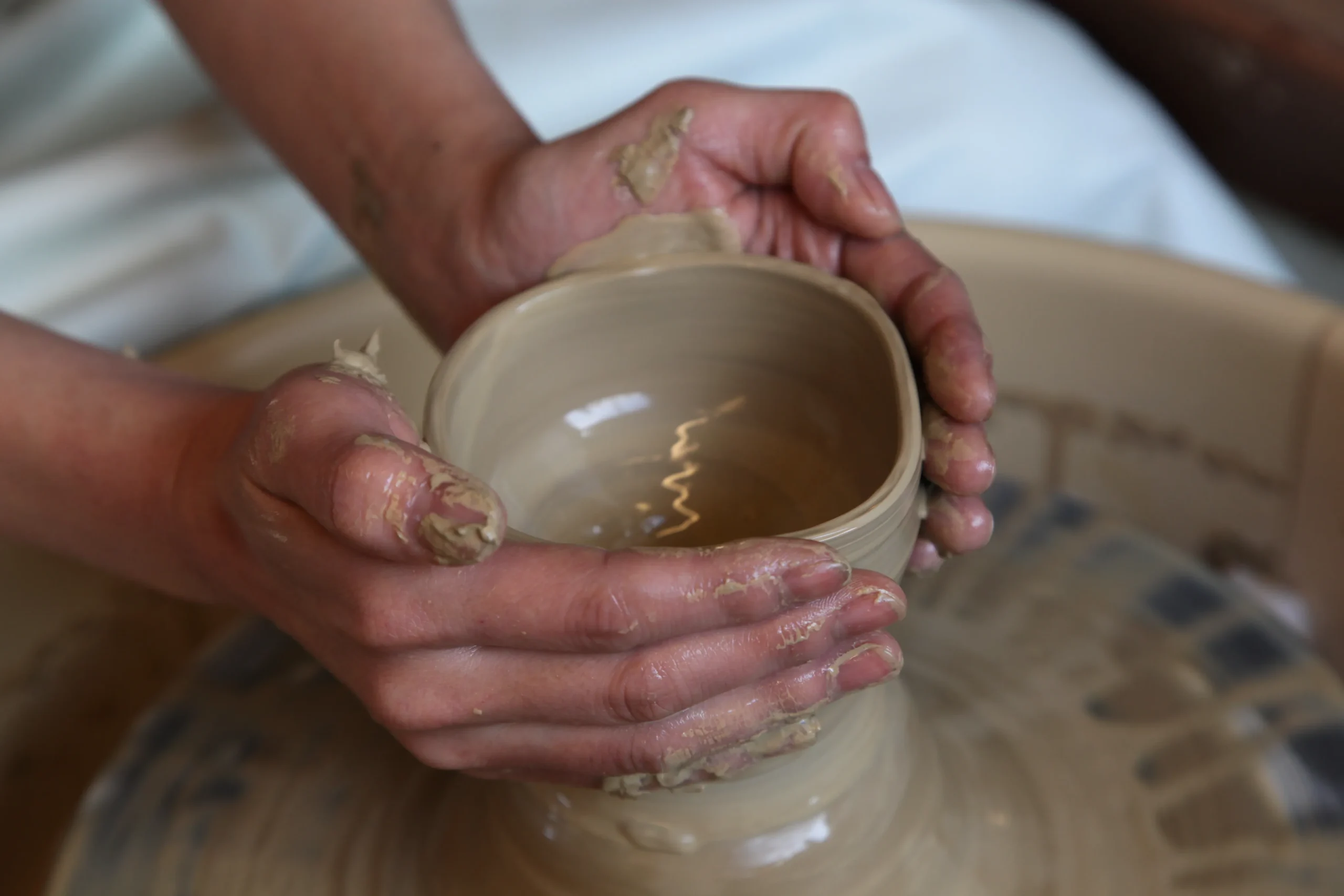 Hands shaping a clay cup on a pottery wheel