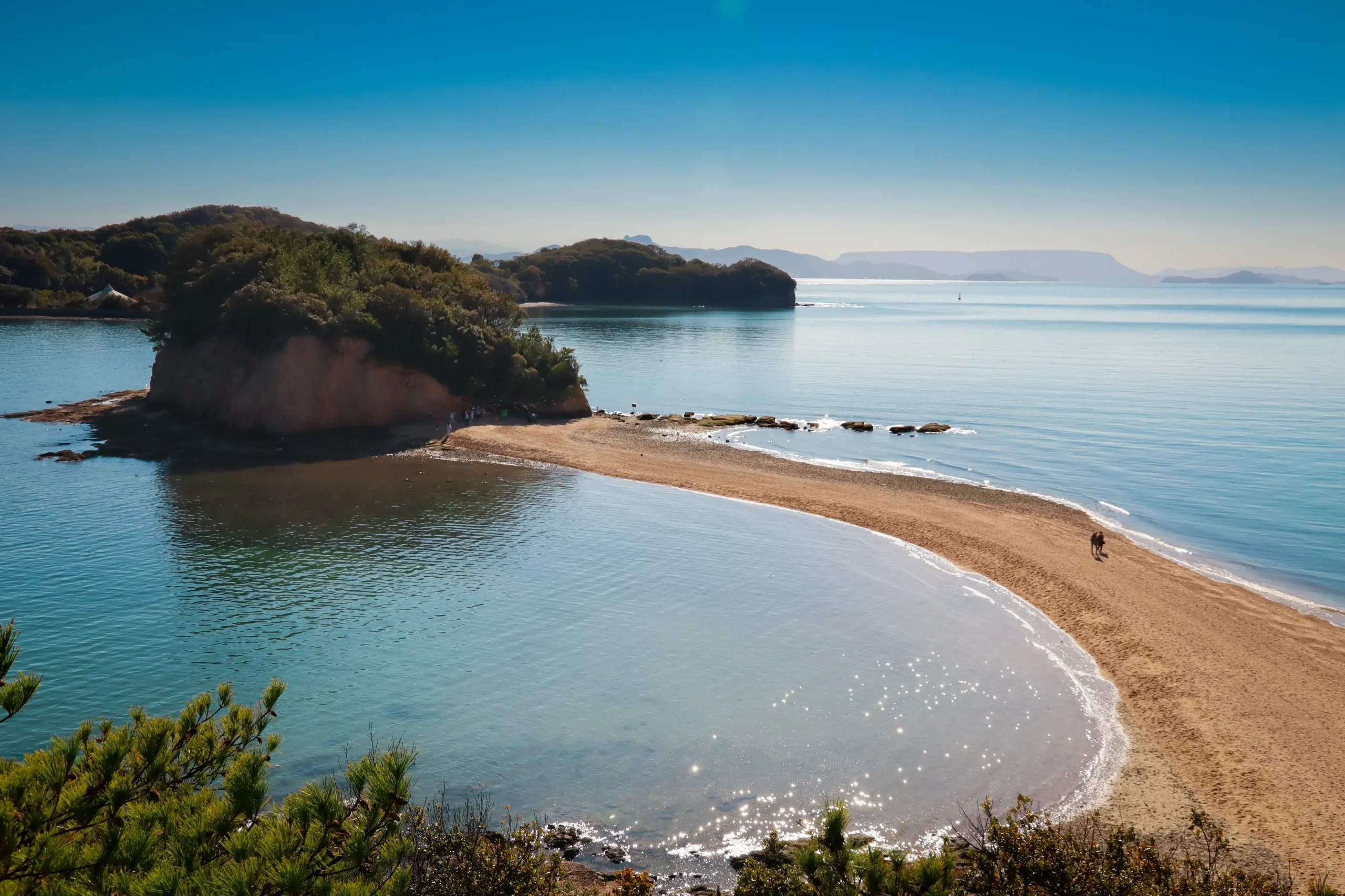 A scenic sandbar connecting small islands during low tide, surrounded by calm blue waters, located in Setouchi, Japan.