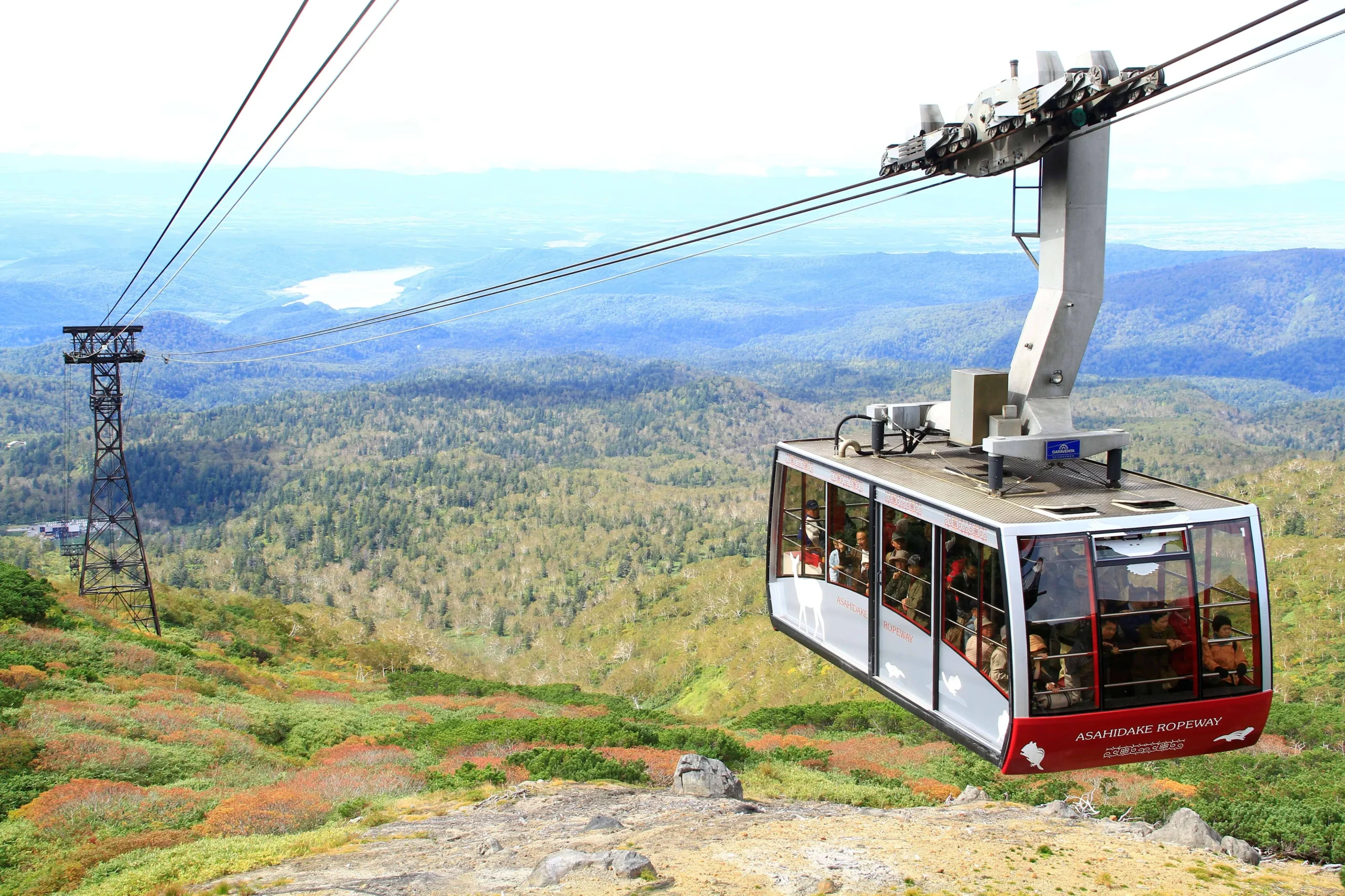 The Asahidake Ropeway cable car ascending over the vast mountainous landscape of Daisetsuzan National Park, offering a panoramic view of nature.