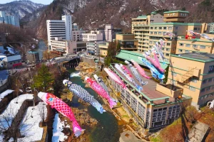 Colorful koi-shaped streamers flying above Jozankei Onsen, with snowy mountains and traditional Japanese inns in the background, symbolizing Children's Day celebrations.