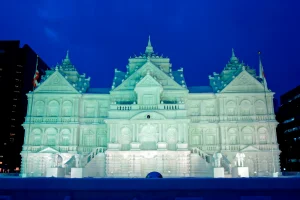 A stunning illuminated snow sculpture of a grand architectural structure, displayed at the Sapporo Snow Festival during the night.