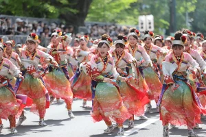 A group of dancers in colorful traditional costumes energetically performing at the YOSAKOI Soran Festival, with a lively crowd cheering in the background.