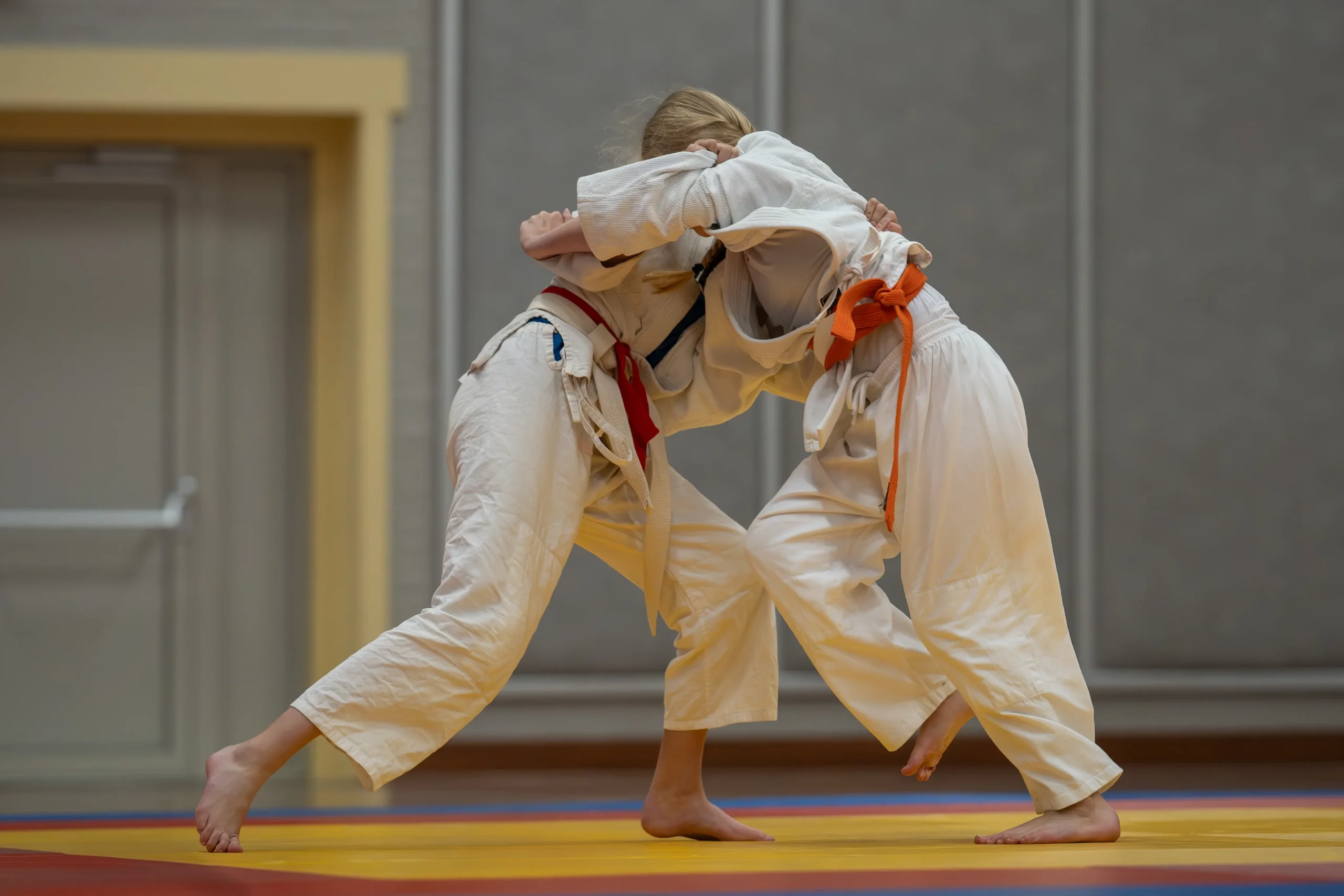 Two judo practitioners in white uniforms gripping each other in a match, demonstrating balance and technique on a tatami mat.