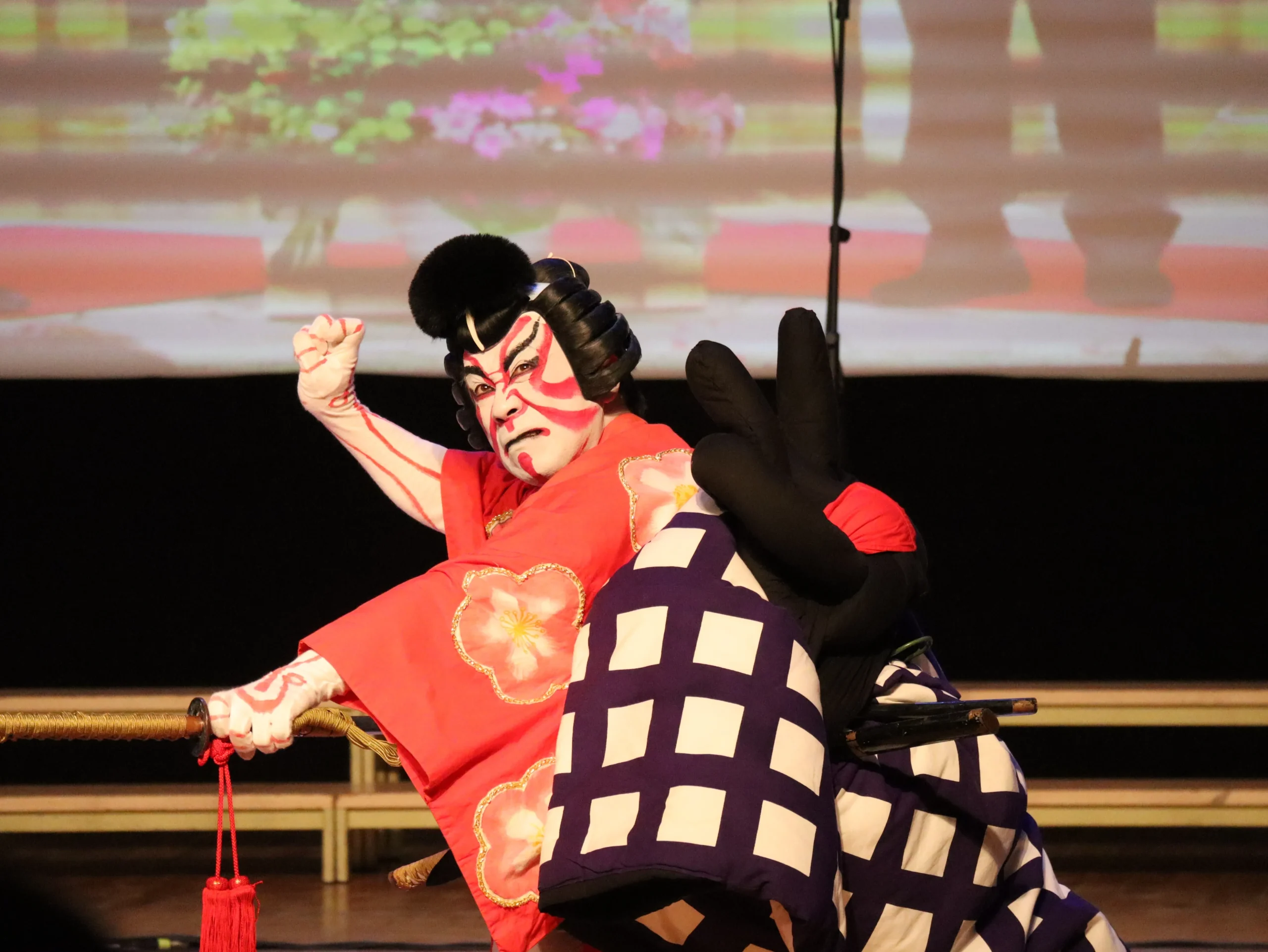 A kabuki actor in a dramatic red and black costume with bold face makeup, striking an intense pose on stage.