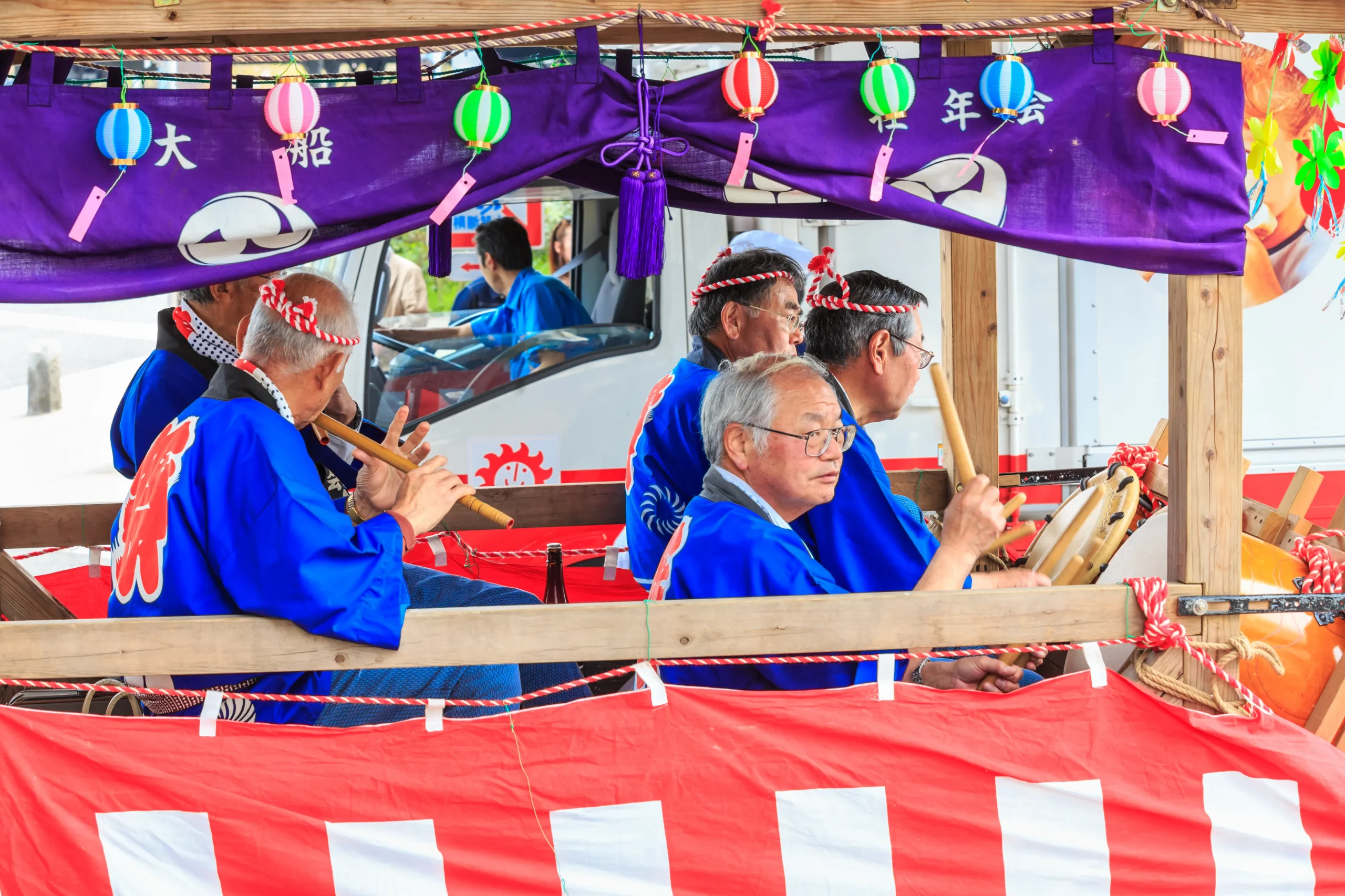 Musicians in traditional blue attire playing flutes and drums on a decorated festival float.