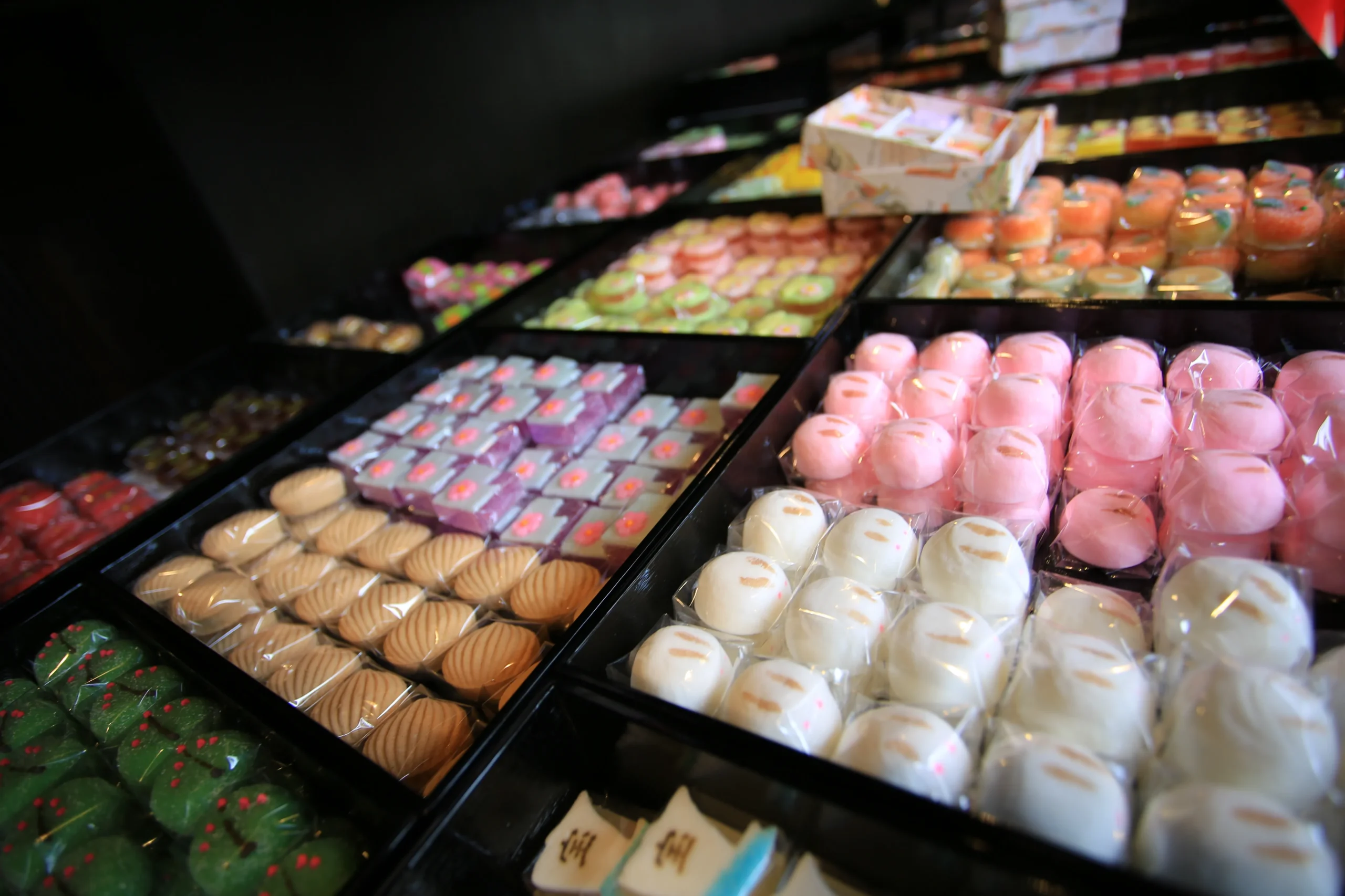 An array of beautifully packaged traditional Japanese wagashi sweets in various colors and shapes, neatly arranged in trays.