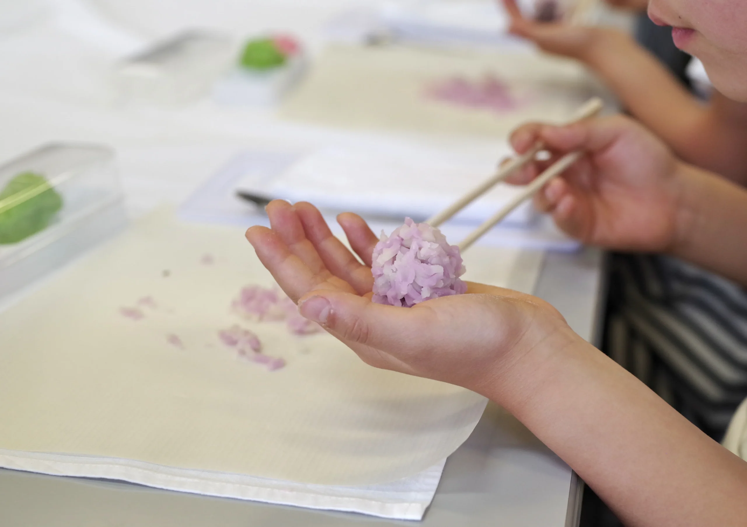 A person shaping delicate Japanese wagashi sweets by hand, using chopsticks to arrange the details.