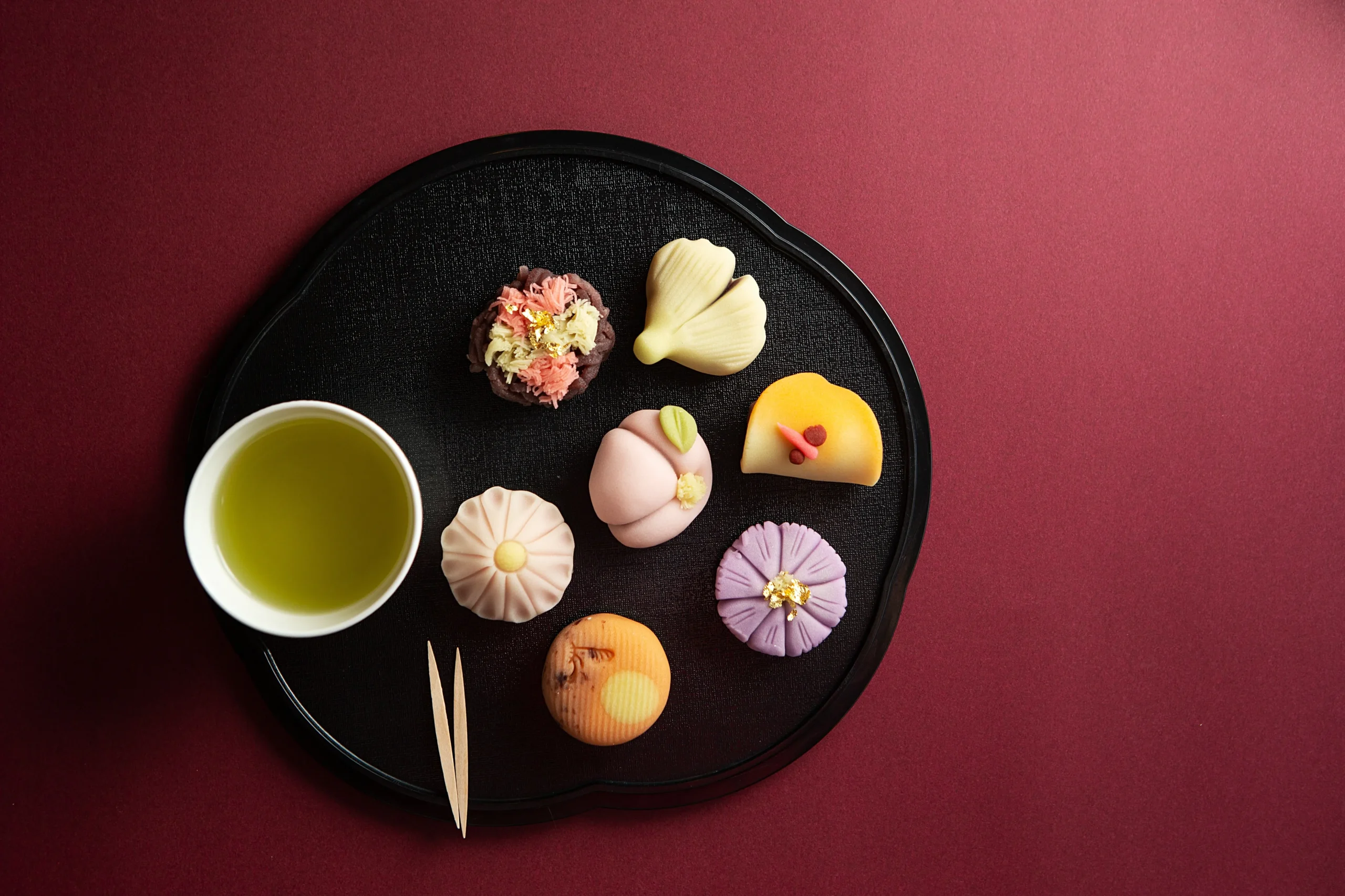 An assortment of beautifully crafted wagashi sweets served with a cup of green tea on a black tray.