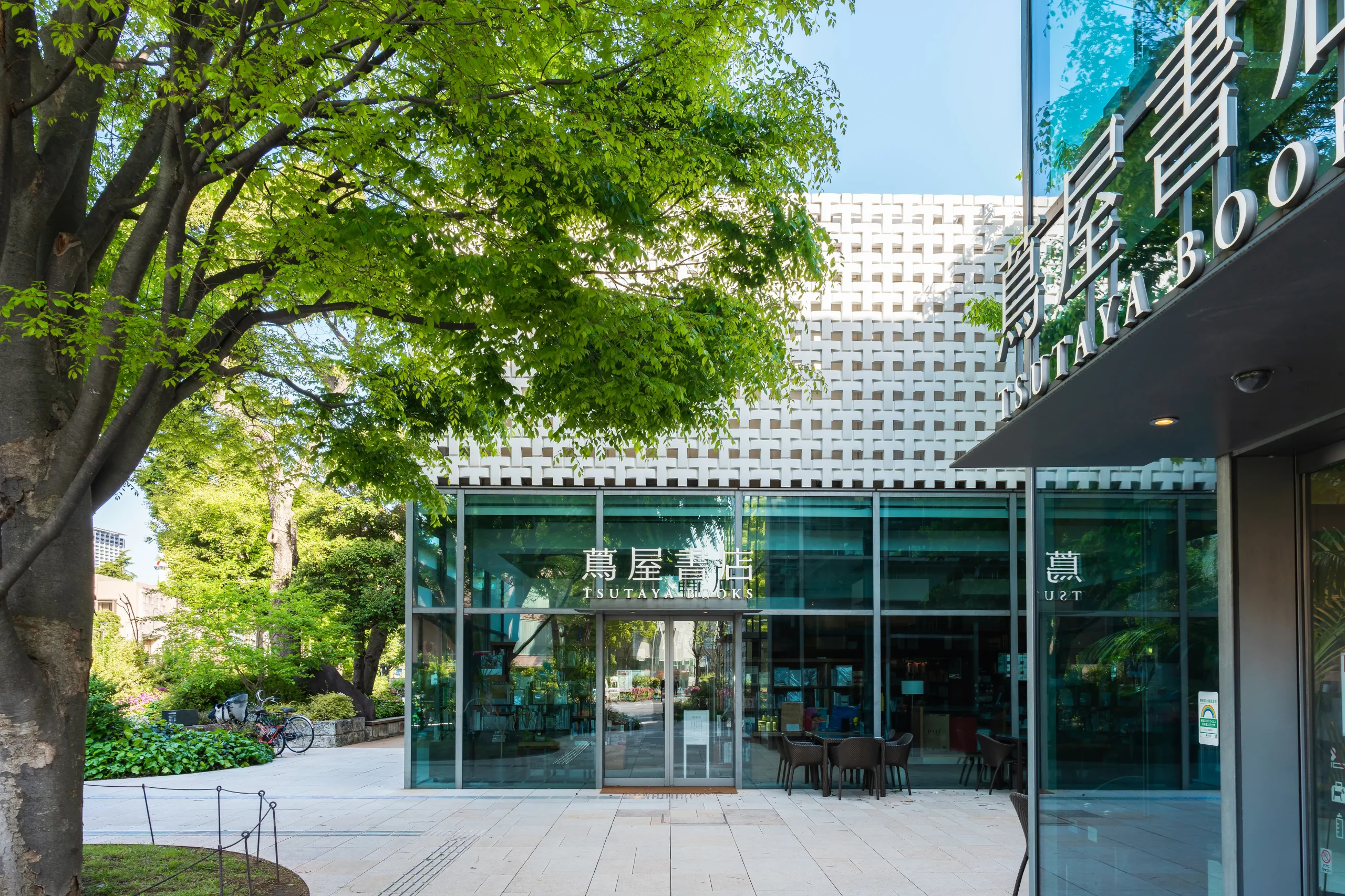 A contemporary bookstore complex surrounded by lush greenery. The glass-walled building reflects the trees, offering a tranquil space for book lovers and café visitors.