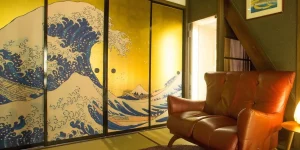 A traditional Japanese-style room featuring a sliding door decorated with a golden reproduction of Hokusai's The Great Wave off Kanagawa, complemented by a cozy leather sofa.