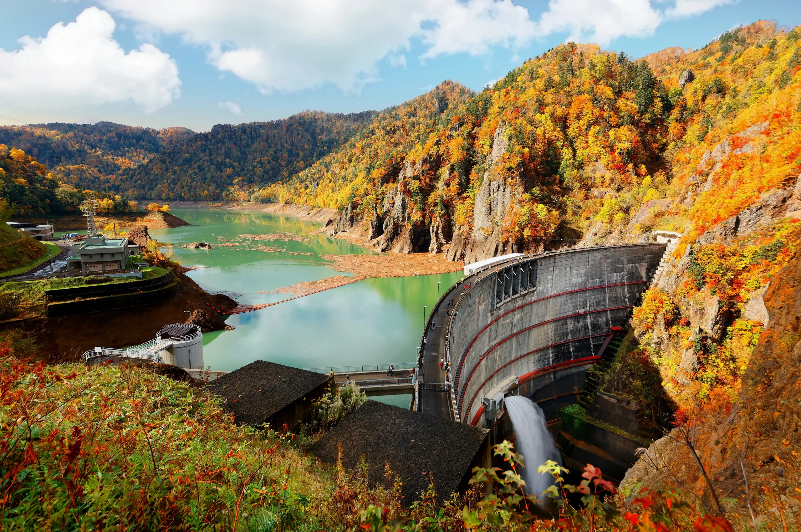 Hoheikyo Dam in autumn, with vibrant fall foliage reflecting in the emerald green water of the reservoir.