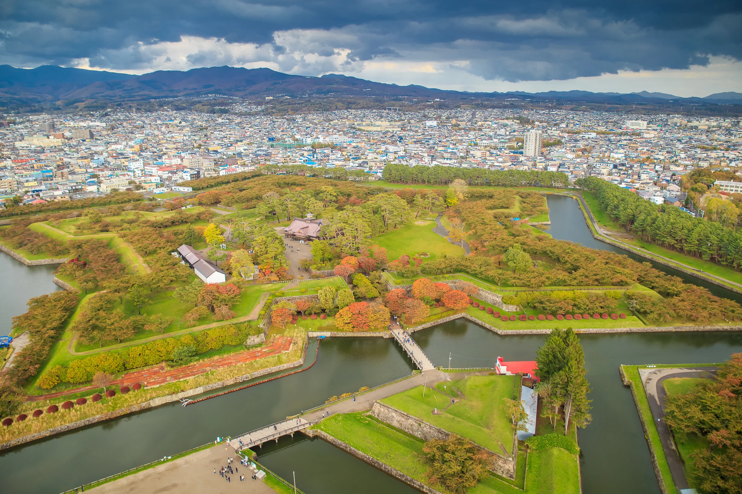 Aerial view of Goryokaku Fort surrounded by warm autumn foliage, with the cityscape of Hakodate in the background.