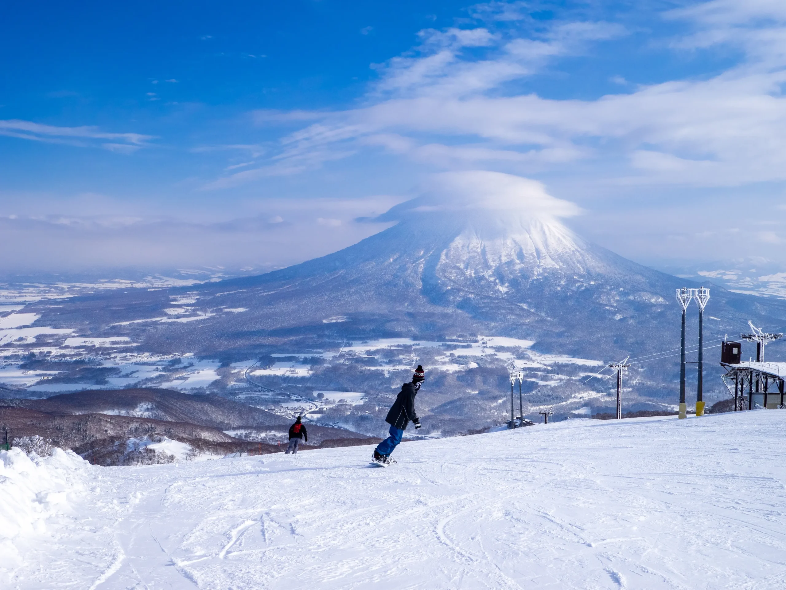 Snowboarders descend the slopes of Niseko with the majestic, snow-capped Mount Yotei rising in the background.