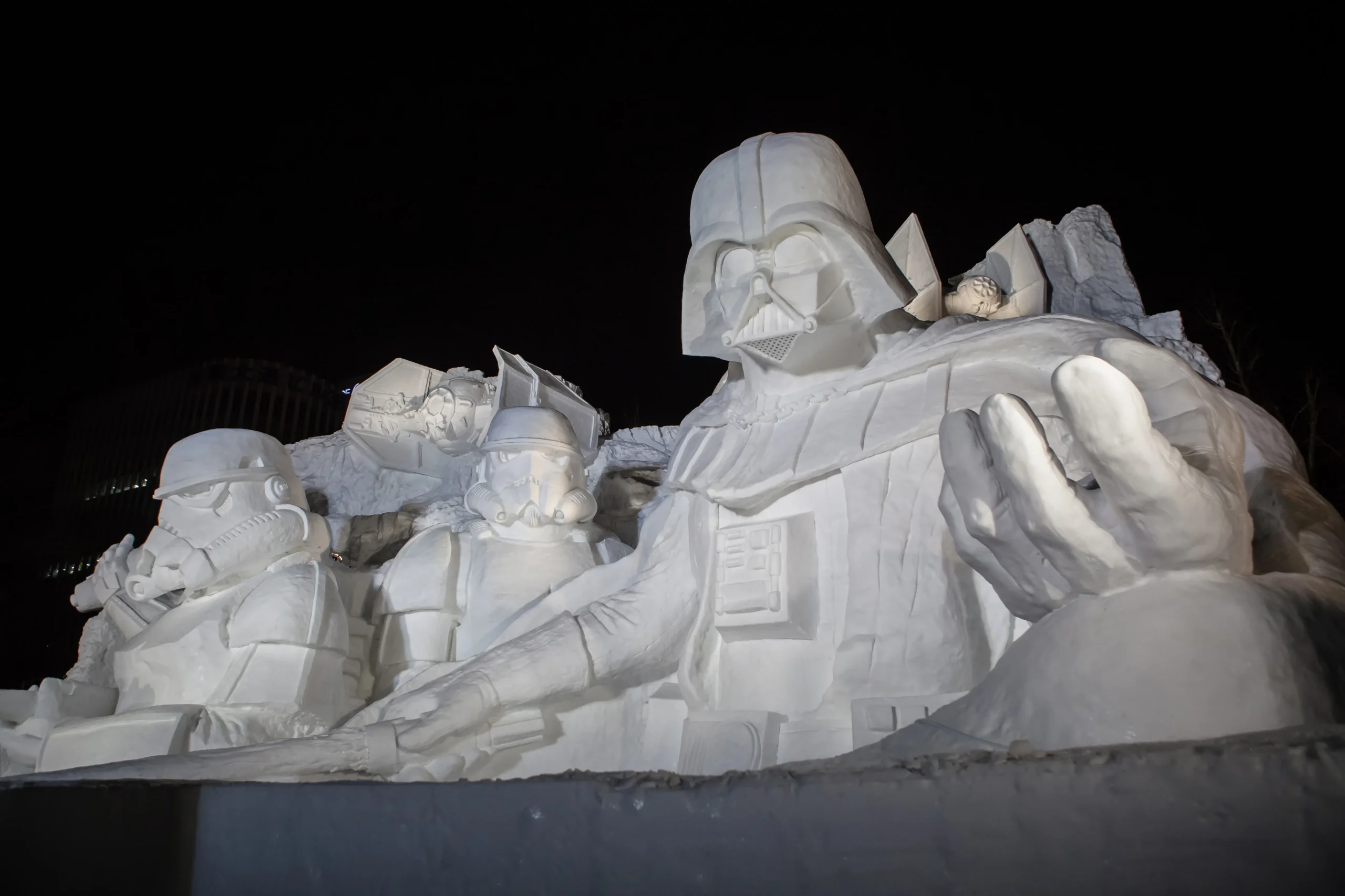 Massive snow sculpture of Darth Vader and Stormtroopers, illuminated at night during the Sapporo Snow Festival in Hokkaido.