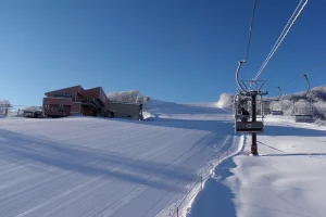 A ski lift ascending a freshly groomed slope under a clear blue sky at Hakuba Goryu Ski Resort in Nagano, Japan.