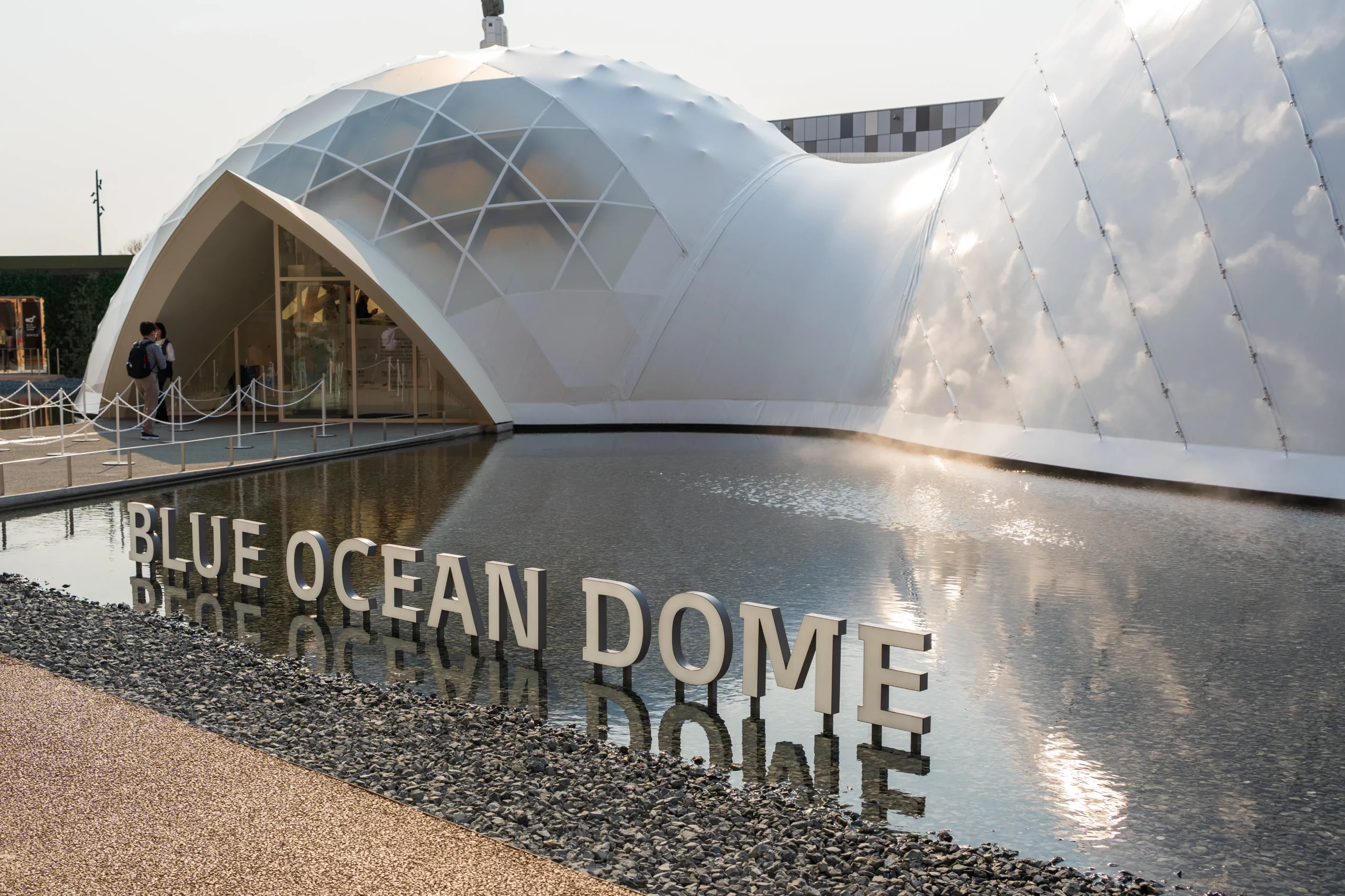 White dome structure labeled “BLUE OCEAN DOME” reflected in a surrounding pool at Expo 2025.