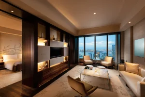 A luxurious hotel suite at Conrad Tokyo featuring a modern living area with elegant furnishings, a separate bedroom, and panoramic city and bay views through floor-to-ceiling windows.