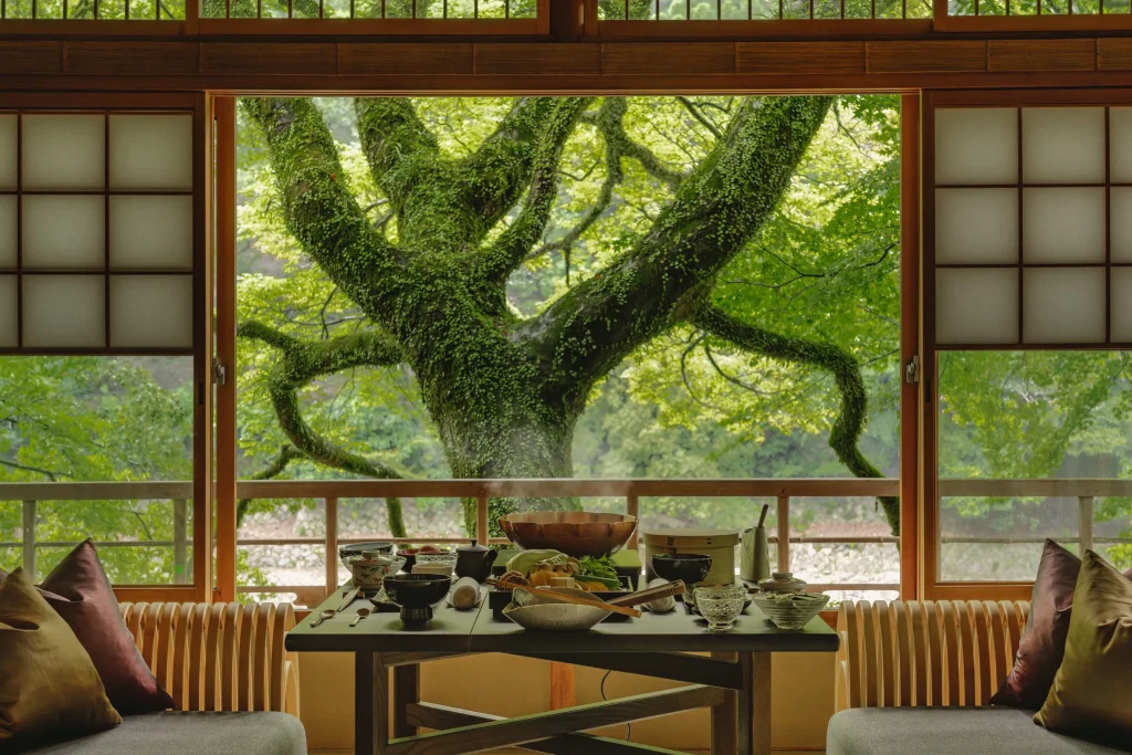 Traditional kaiseki meal served in a riverside room at HOSHINOYA Kyoto with a view of mossy trees.