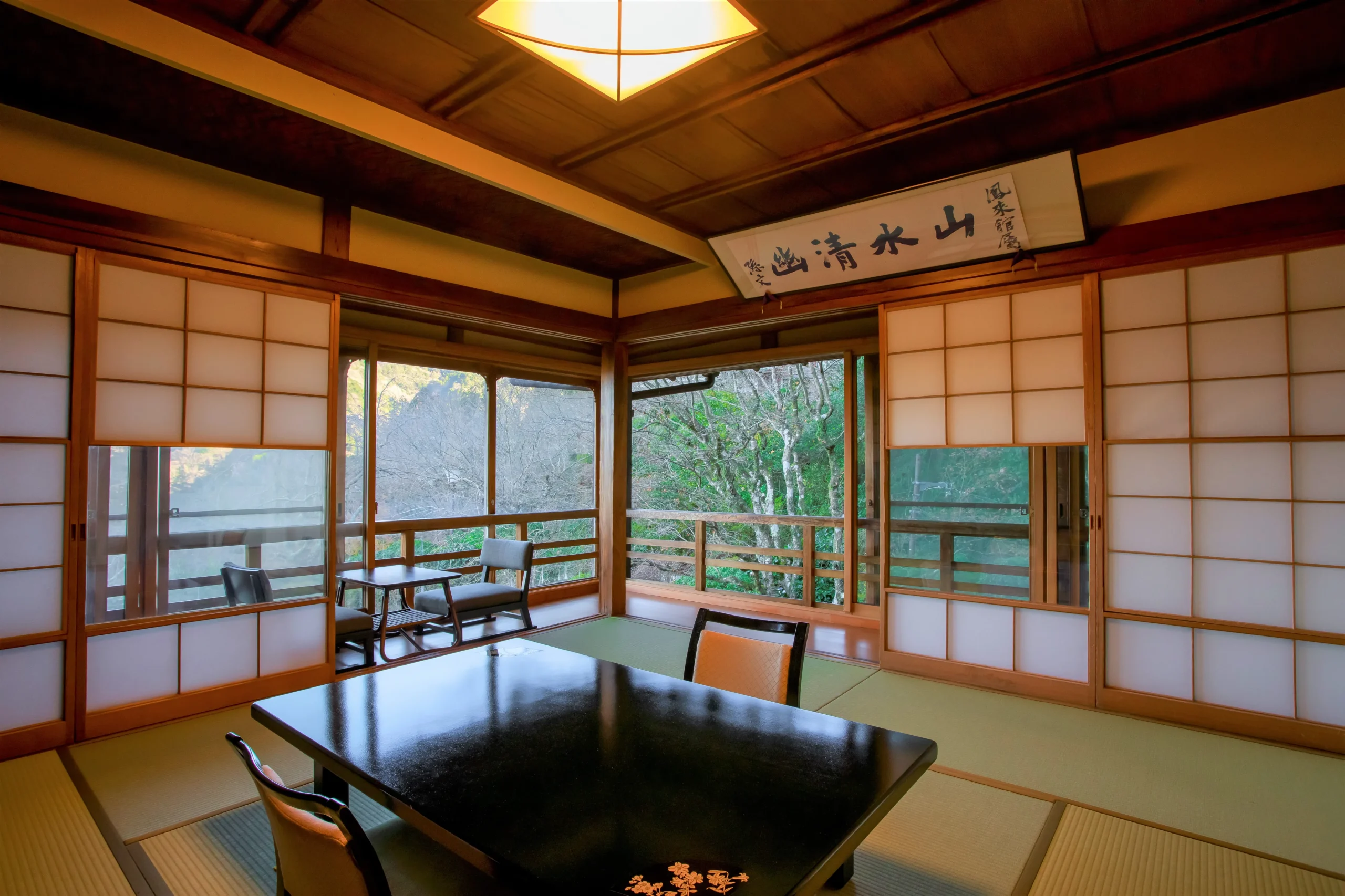 Traditional Japanese-style tatami room at Mikawaya Ryokan, with shoji doors, a low dining table, and scenic mountain views through wide windows.