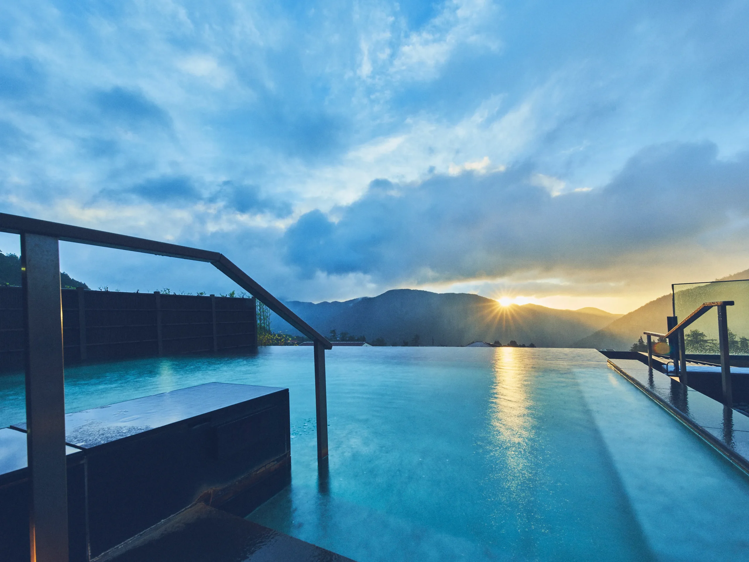 Outdoor infinity onsen bath at Hakone Kowakien Tenyu, overlooking mountain ridges at sunset under a dramatic sky.