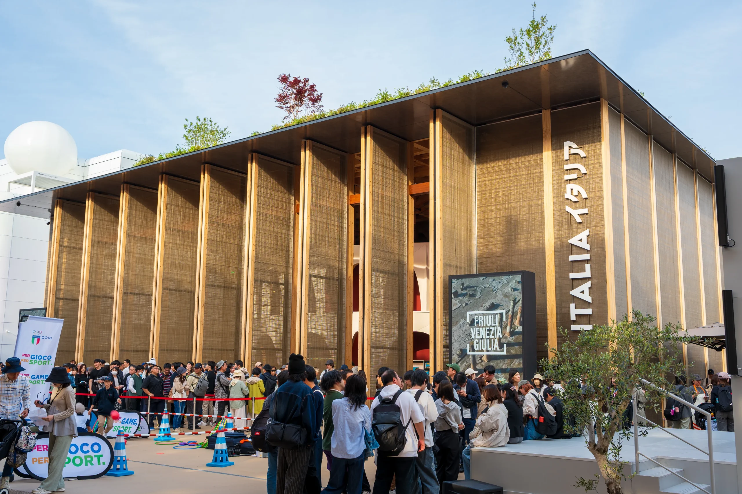 Modern wooden Italy Pavilion with a green rooftop garden and a large crowd waiting to enter.