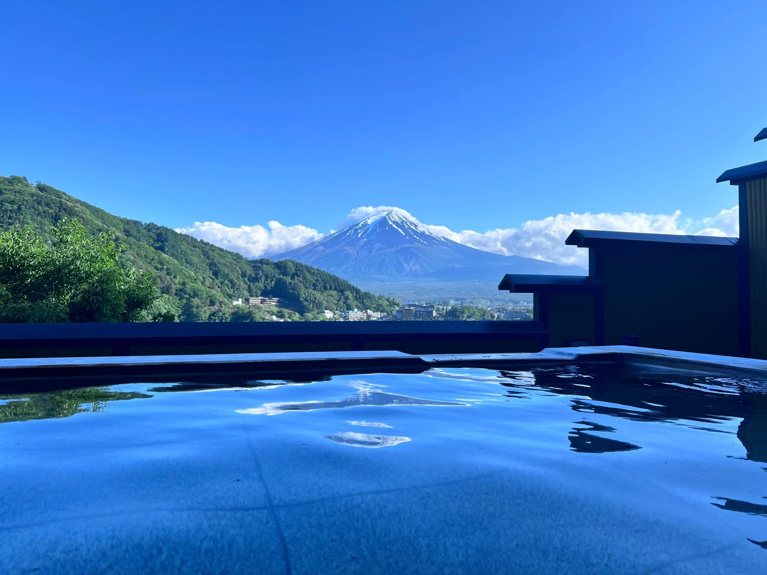 A peaceful outdoor hot spring bath with a scenic view of Mount Fuji and surrounding green hills.
