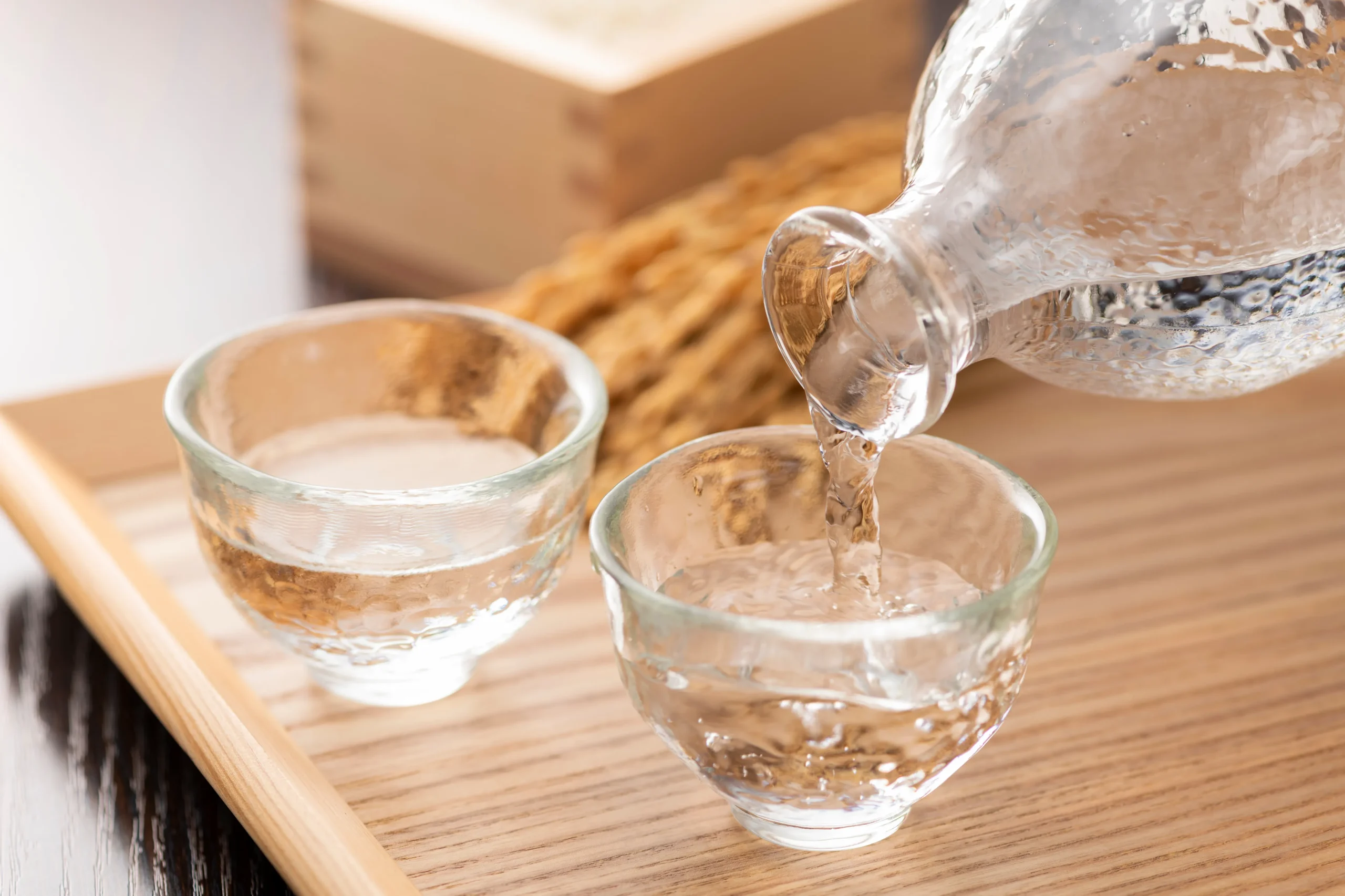 Pouring Japanese sake into traditional glass cups on a wooden tray