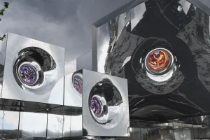 Futuristic mirrored pavilion with swirling, lens-like designs reflecting the sky at Expo 2025.