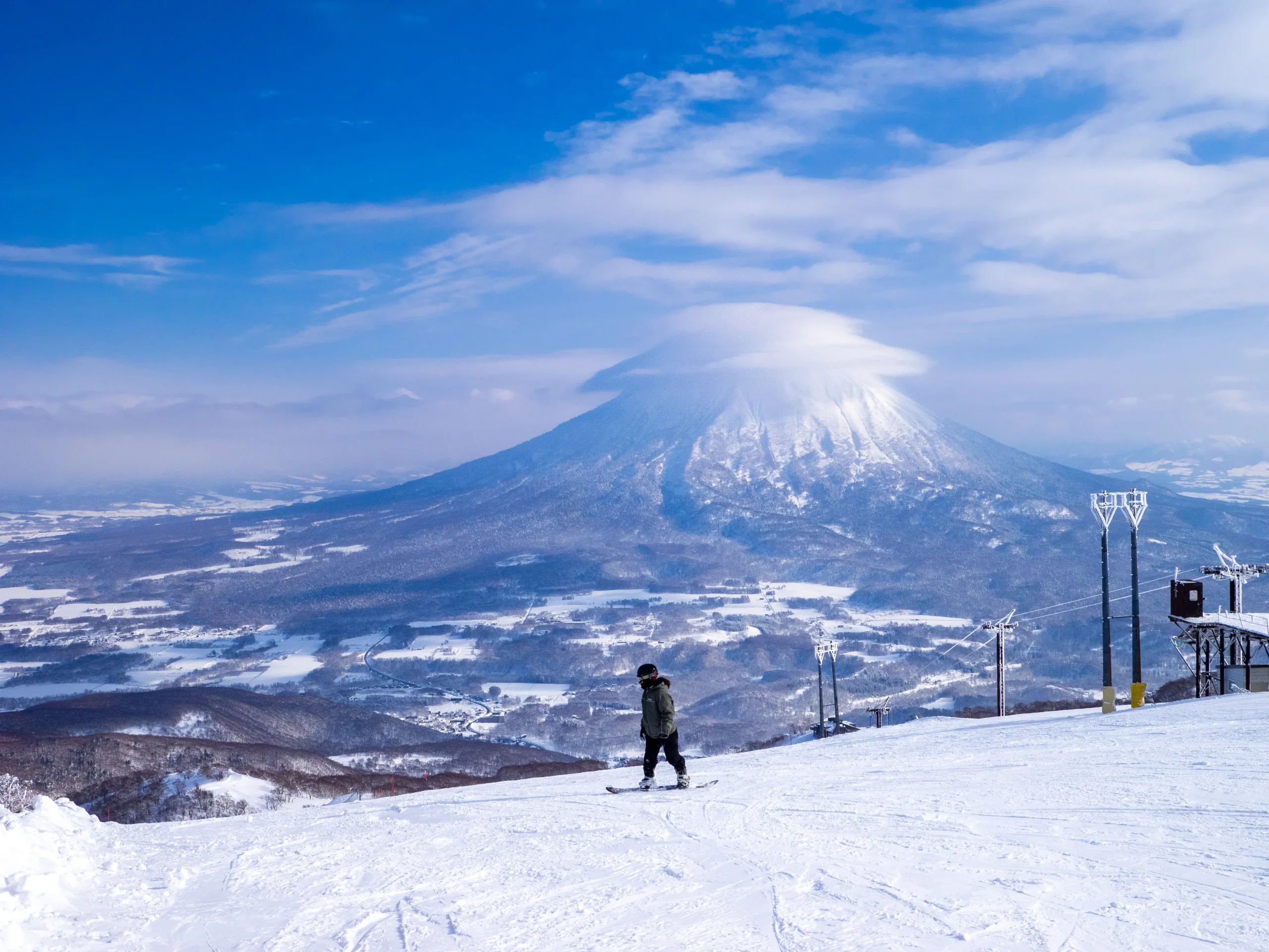 A lone snowboarder overlooking a vast snowy valley with Mount Yotei in the background at Niseko.