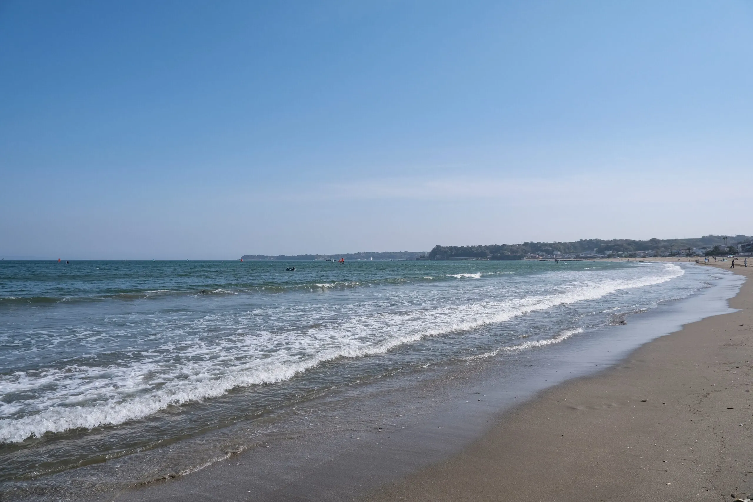A quiet beach along Tokyo Bay with gentle waves lapping the shore under a clear blue sky.