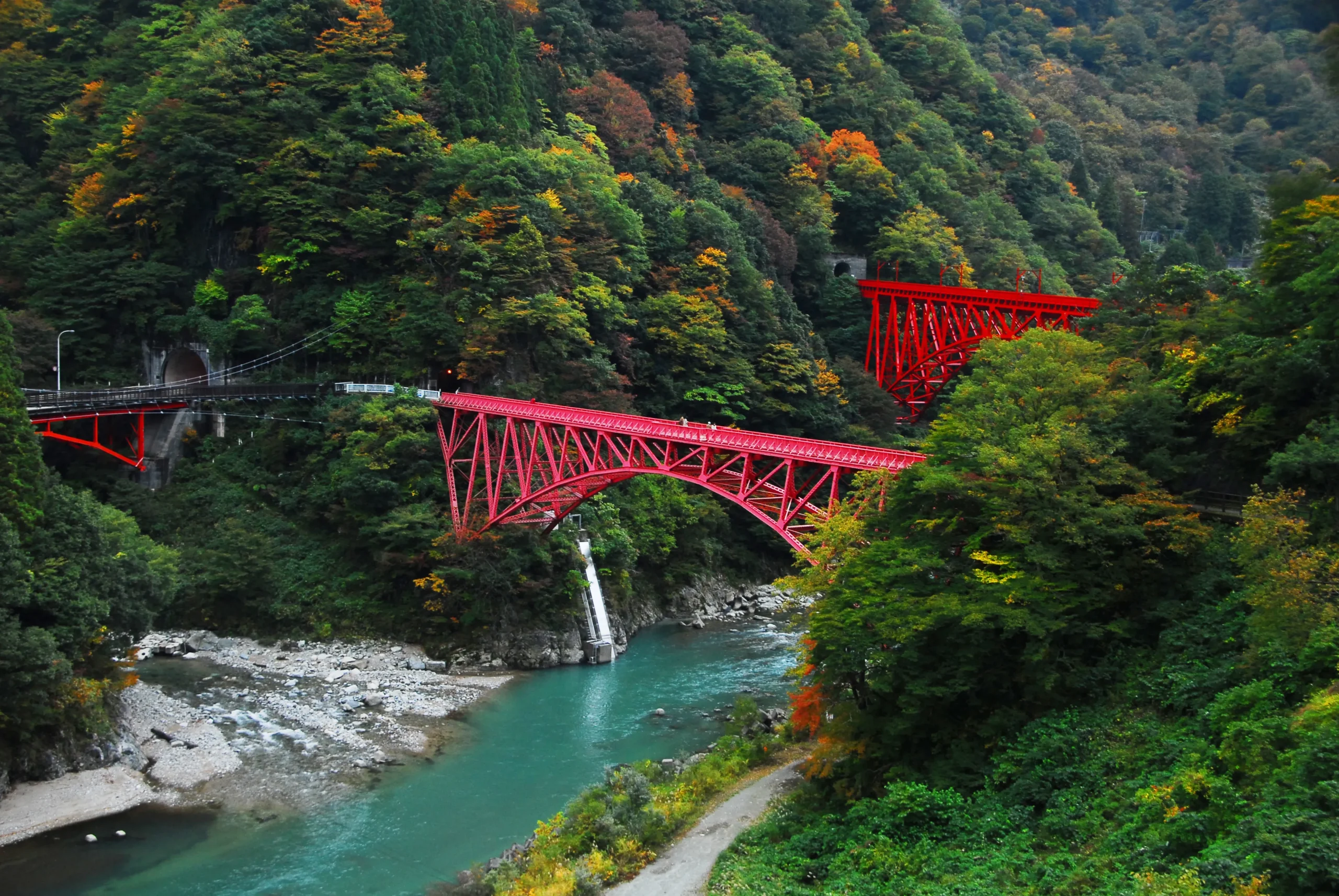Kurobe Gorge Railway crossing a vivid red bridge over a turquoise river in autumn