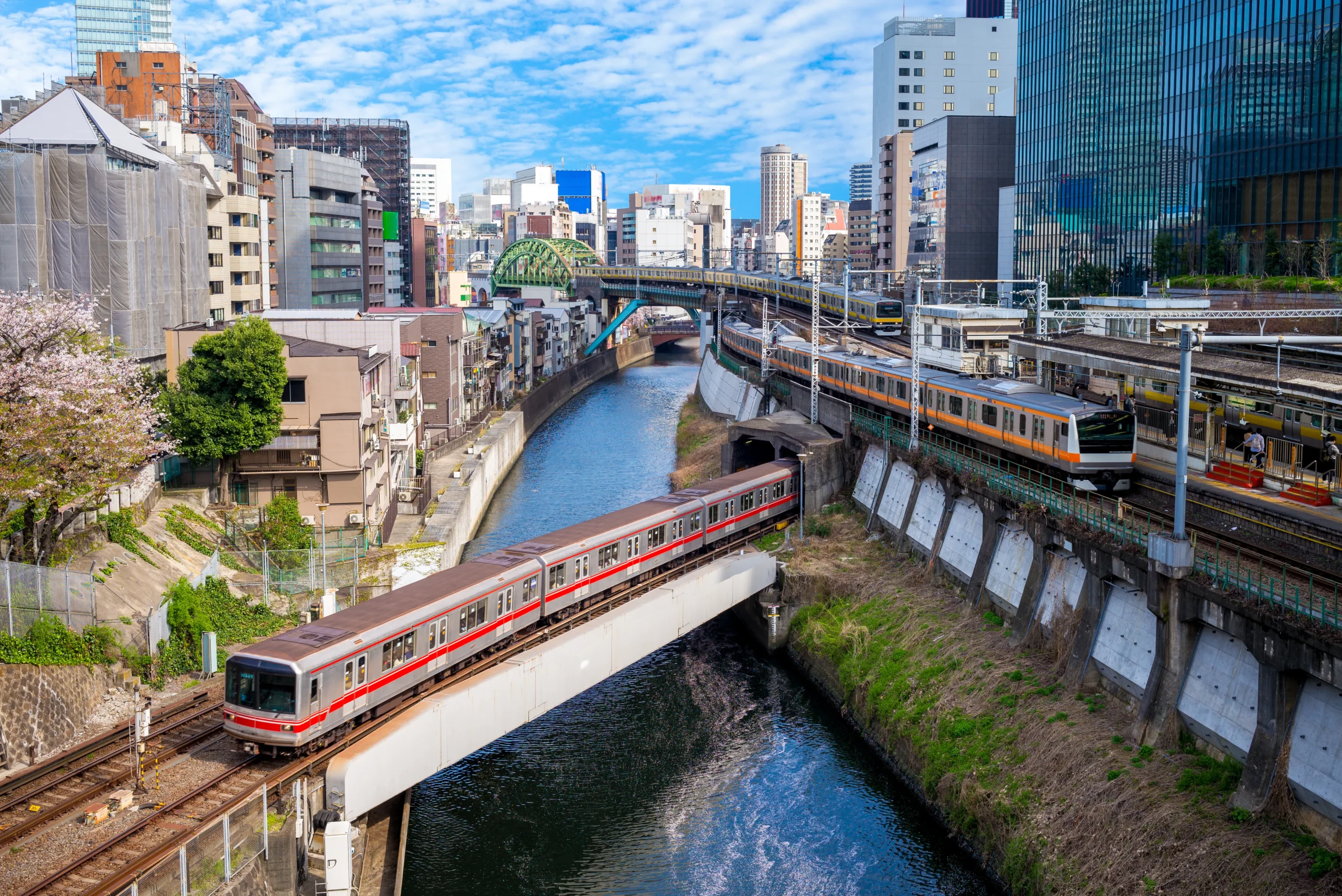 Local trains crossing river in central Tokyo, Japan, urban rail scene with city skyline