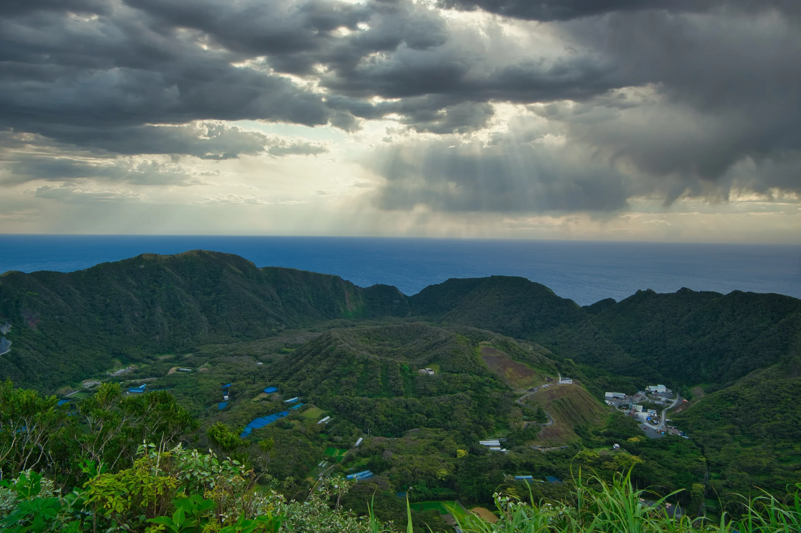 Sunlight breaking through clouds over the double caldera of Aogashima Island.