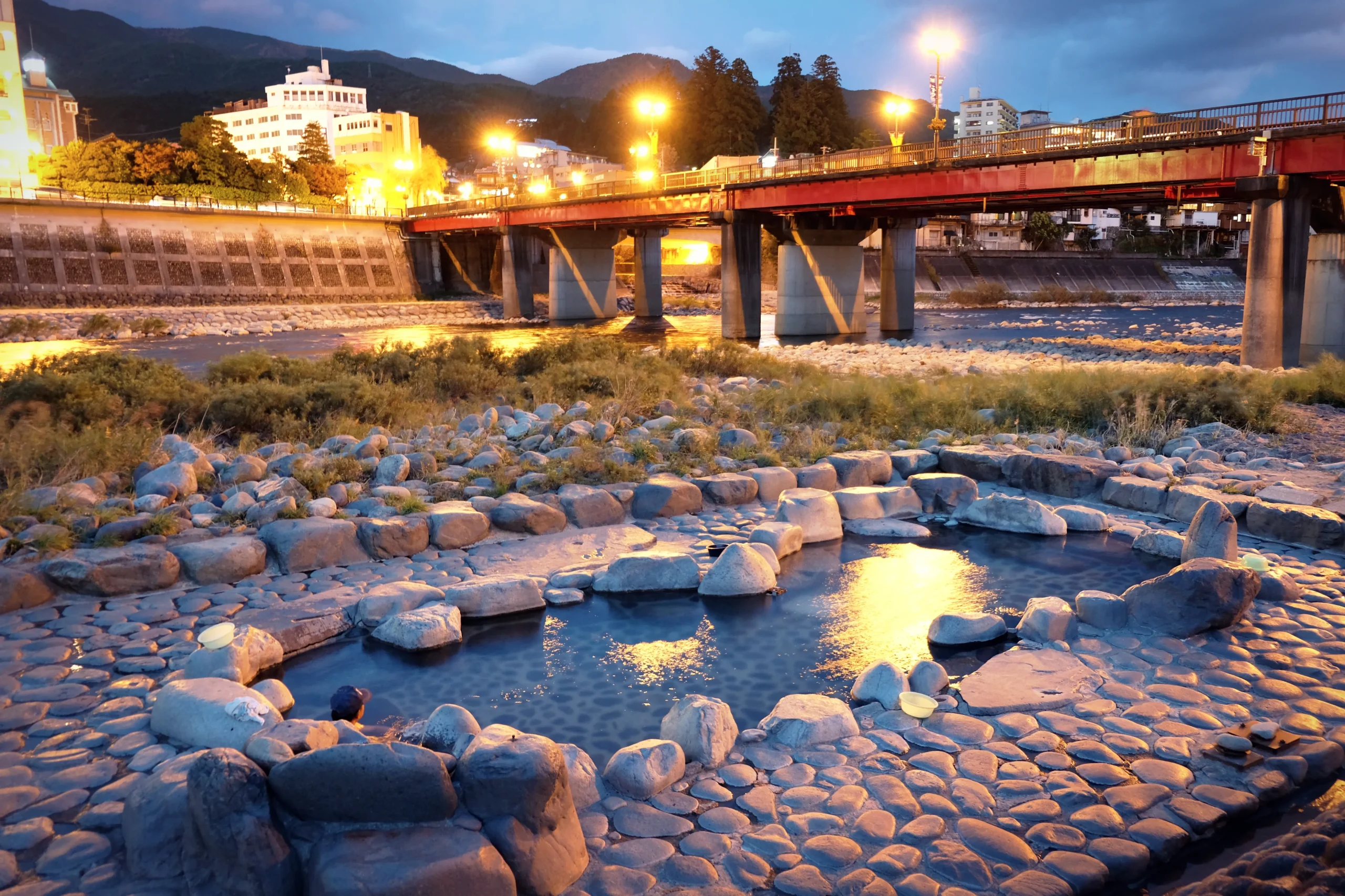 Outdoor public hot spring bath by the Hida River at twilight in Gero Onsen.